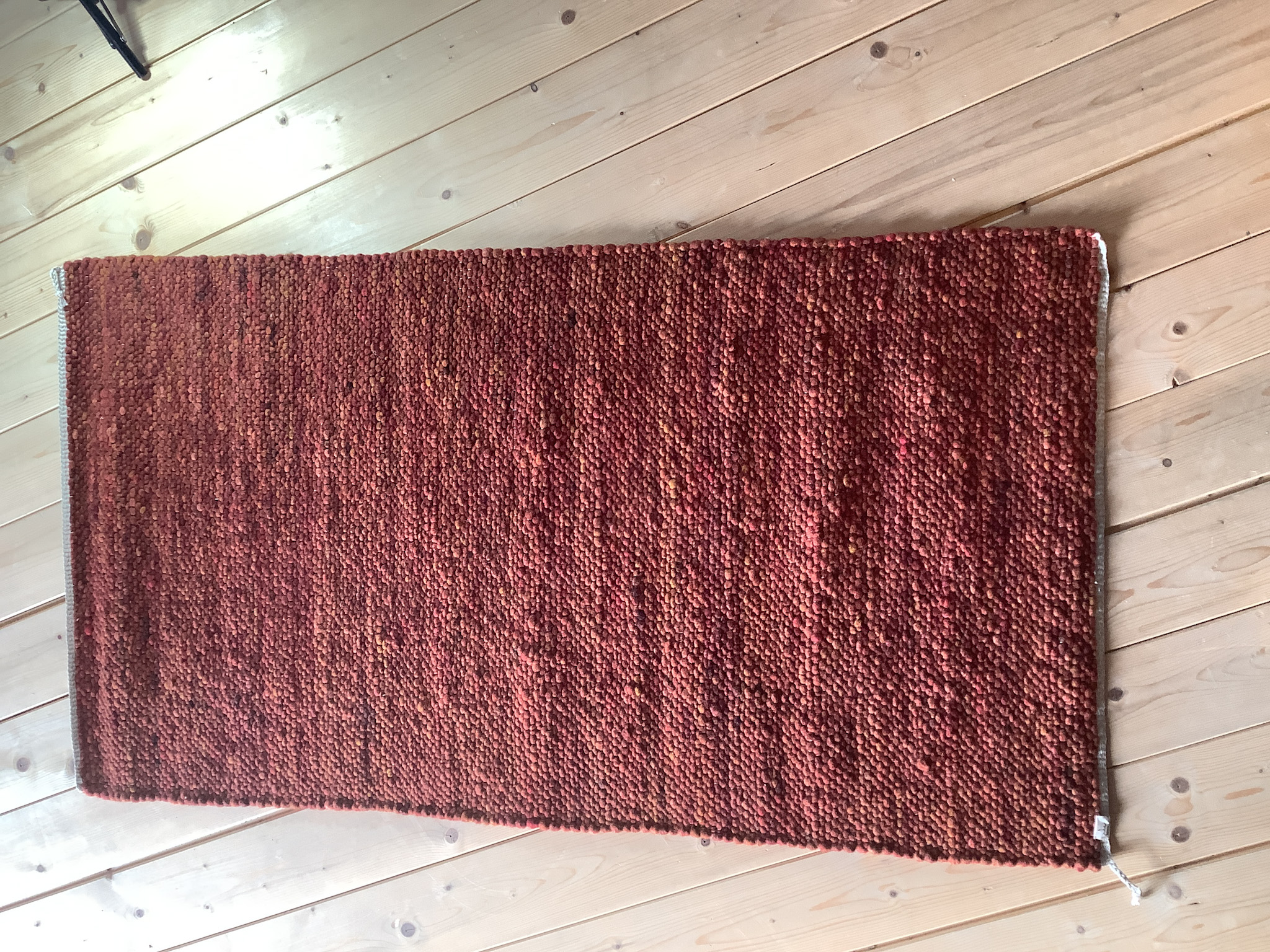 Rechteckiger, rot melierter Wollteppich in dichter Handweboptik, liegend auf hellem Holzboden