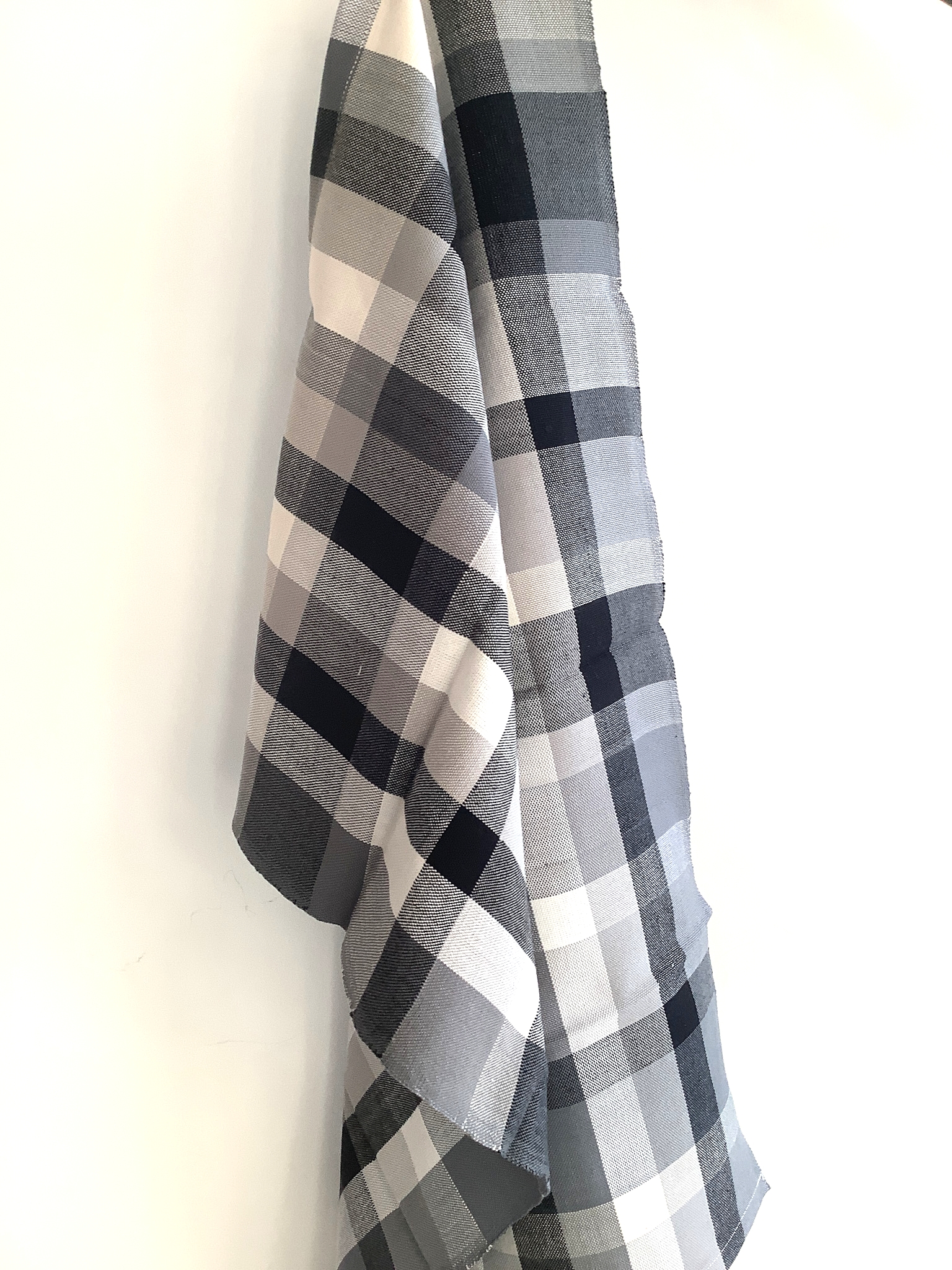 Aufgehängtes kariertes Küchenhandtuch in Grau- und Schwarztönen aus Baumwolle vor weißem Hintergrund