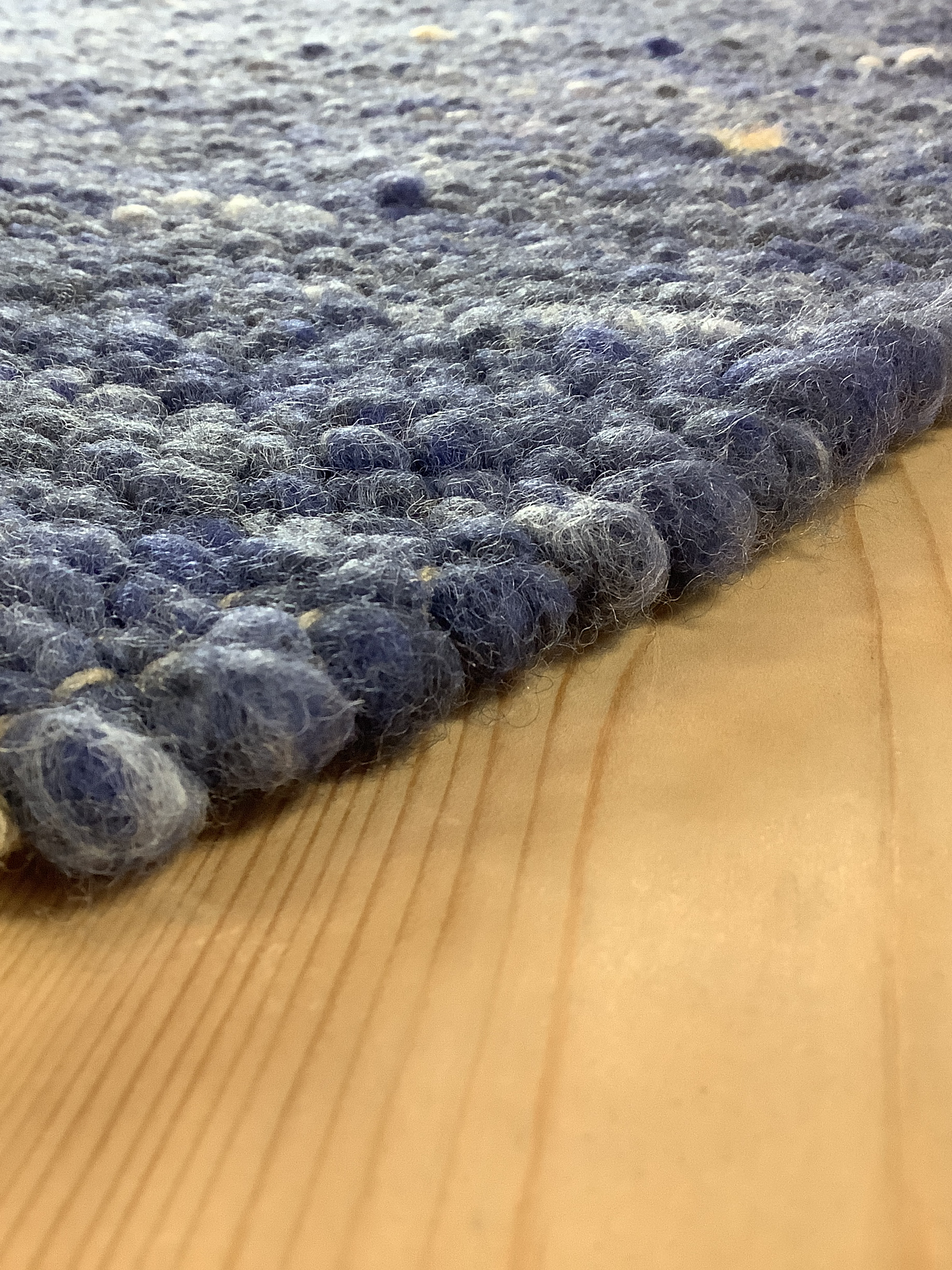 Detailaufnahme eines blauen Filzteppichs mit grob geknüpfter Oberfläche auf hellem Holzfußboden
