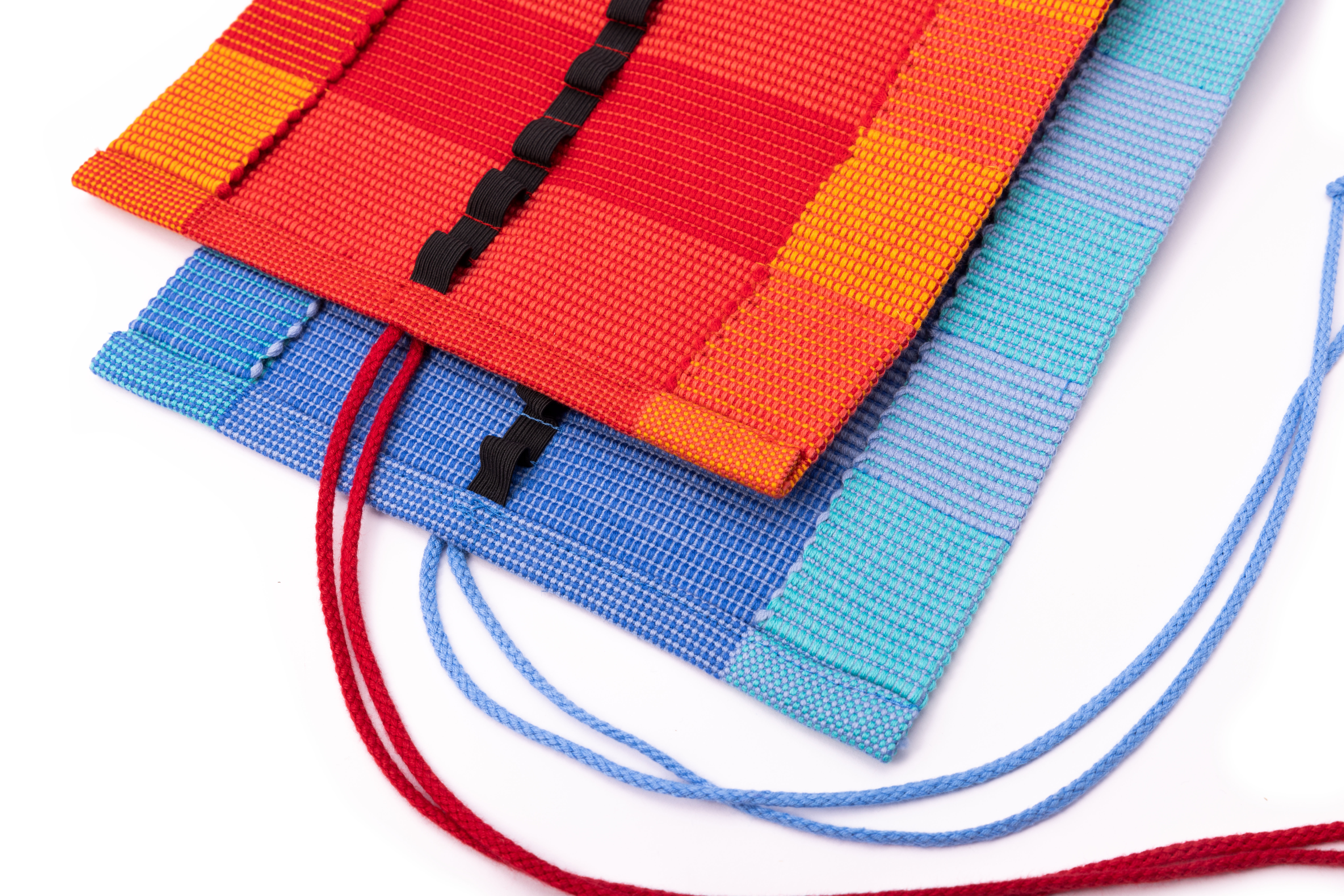 Bunte gewebte Stofftaschen mit Schnüren Zwei farbige gewebte Stofftaschen, eine in Rot-Orange und eine in Blau mit Schnüren, auf einem weißen Hintergrund