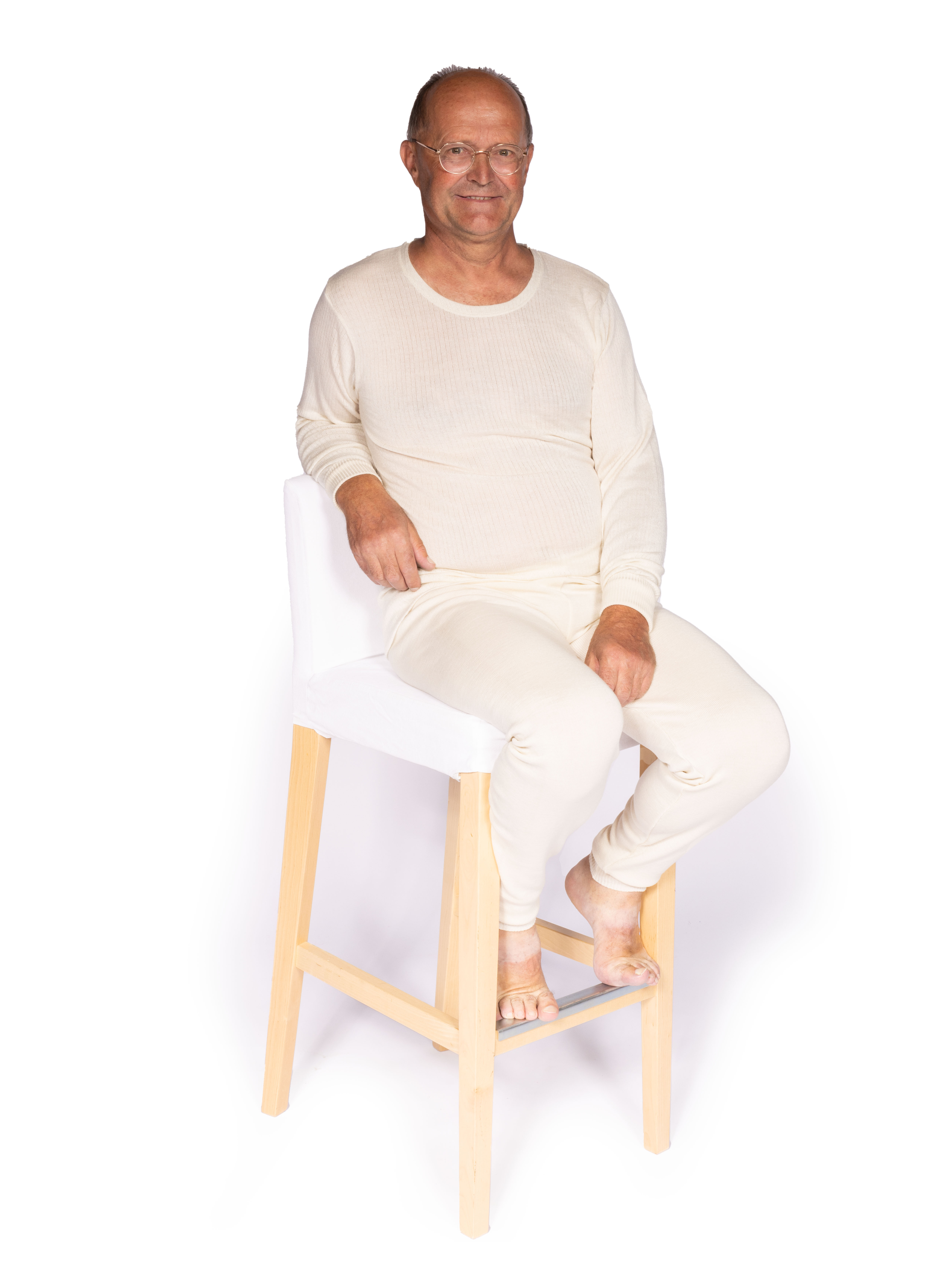 Mann in bequemer Thermo-Unterwäsche auf einem Barhocker Älterer Mann sitzt auf einem Holz-Barhocker und trägt cremefarbene Thermo-Unterwäsche