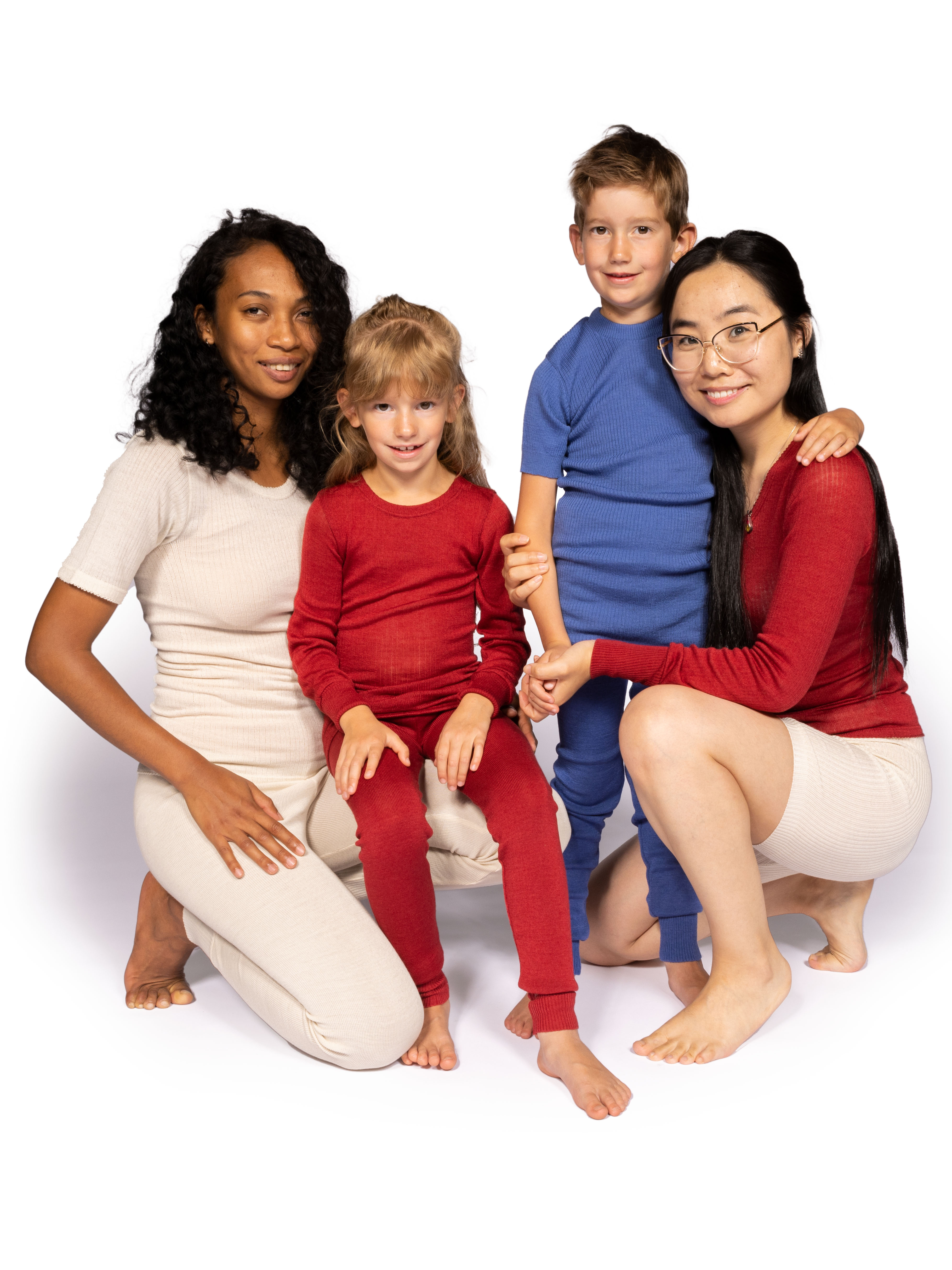 Vier Personen in bequemer Homewear sitzen zusammen auf dem Boden, zwei Frauen und zwei Kinder in farblich abgestimmten Outfits