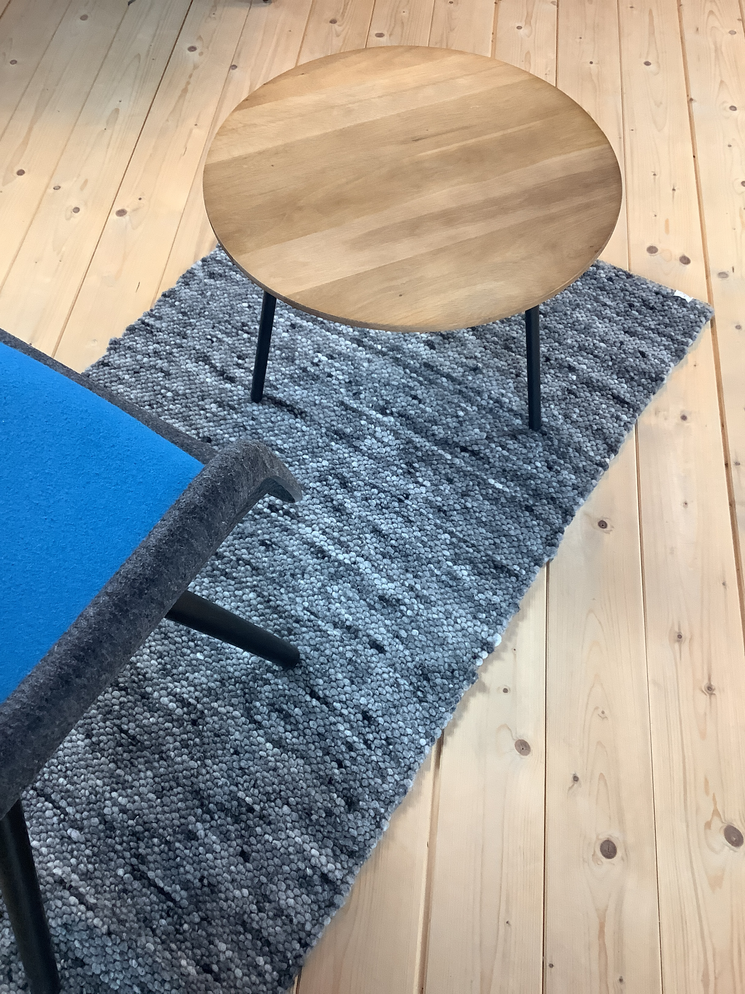Moderner runder Holztisch auf grauem Teppich Ein runder Holztisch steht auf einem grauen Teppich, daneben ein blauer Stuhl, auf einem Holzboden.