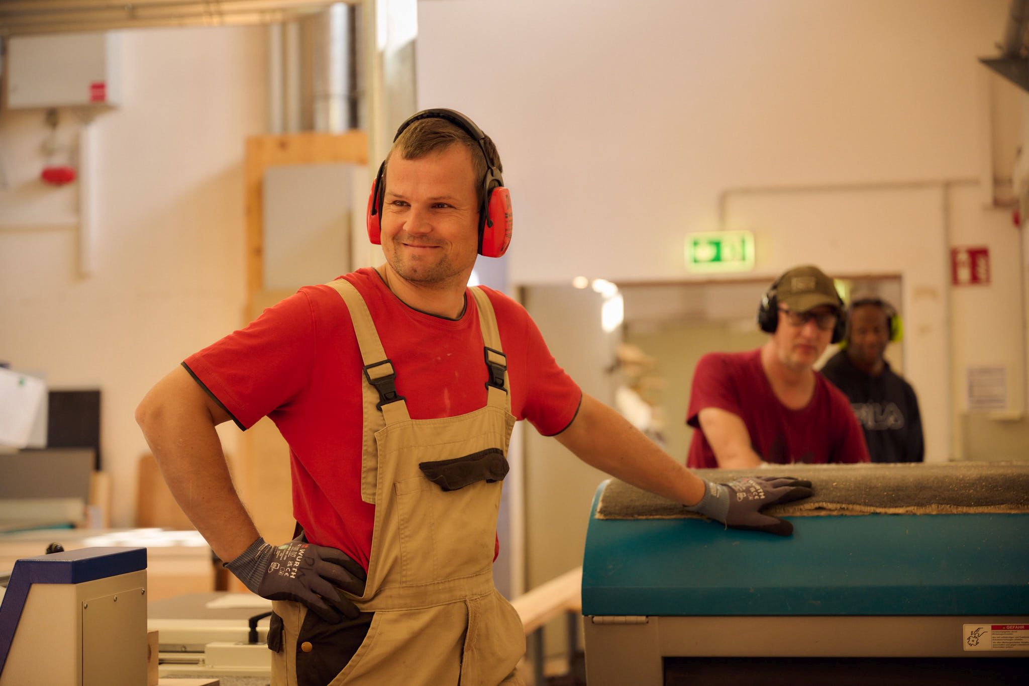 Tischler in Werkstatt bei der Holzverarbeitung Ein Tischler in rotem T-Shirt und Latzhose arbeitet in einer Holzwerkstatt mit Gehörschutz.
