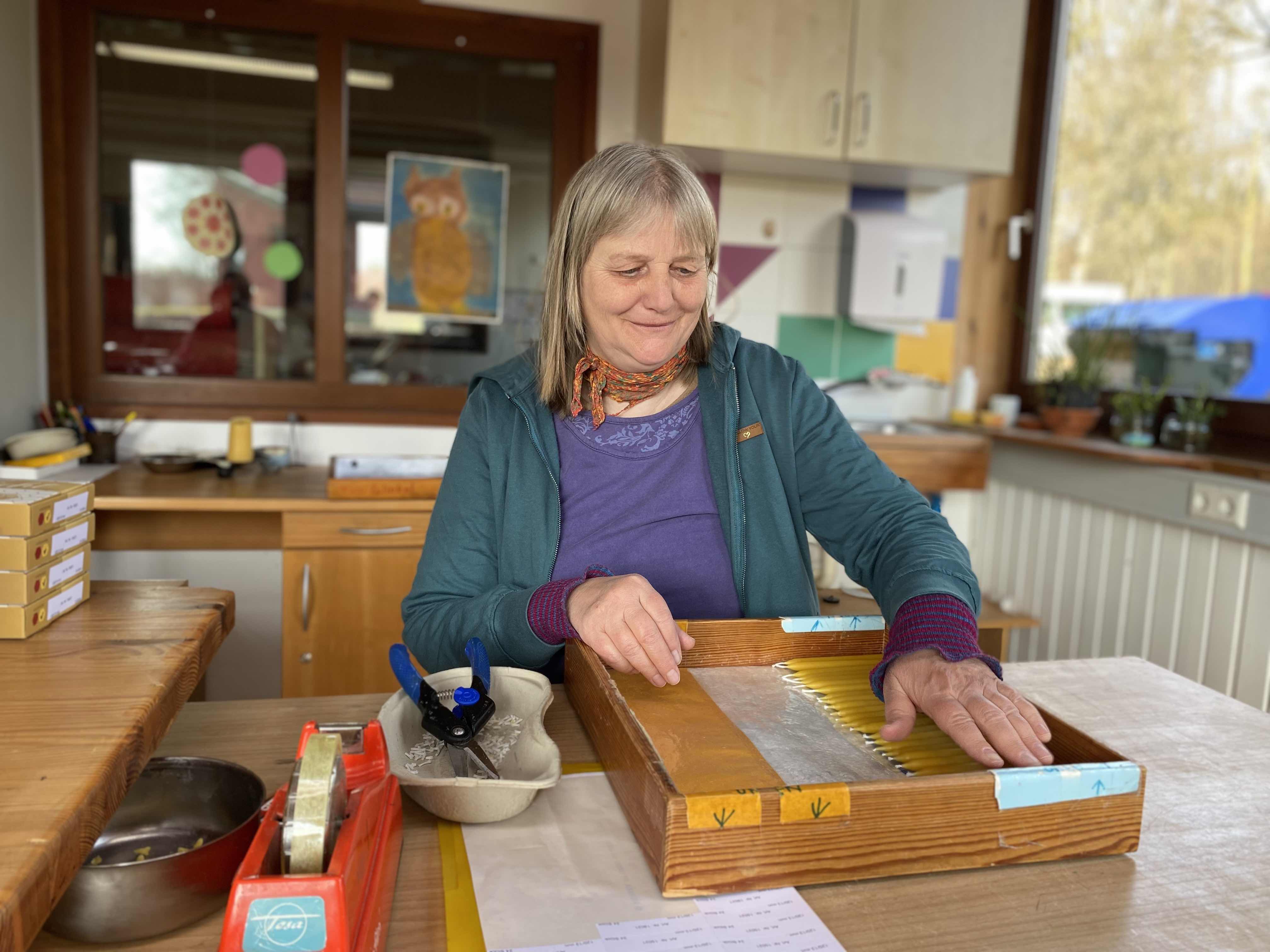 Frau bei der Arbeit mit Bienenwachs in einer Werkstatt Eine Frau in einer Werkstatt, die mit Bienenwachs arbeitet, umgeben von Werkzeugen und Materialien auf einem Tisch.