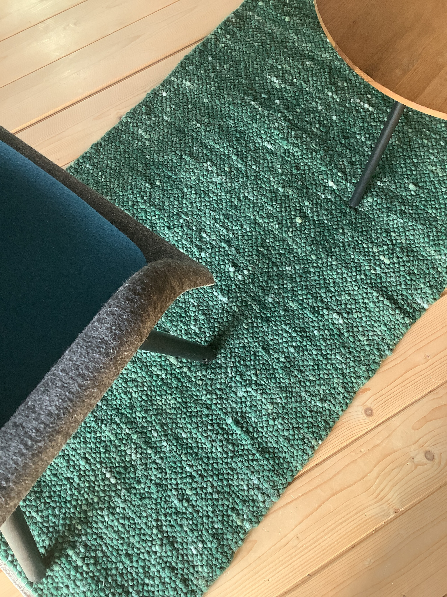 Detailansicht eines grünen, grob gewebten Teppichläufers auf hellem Holzboden mit Stuhl- und Tischbeinen