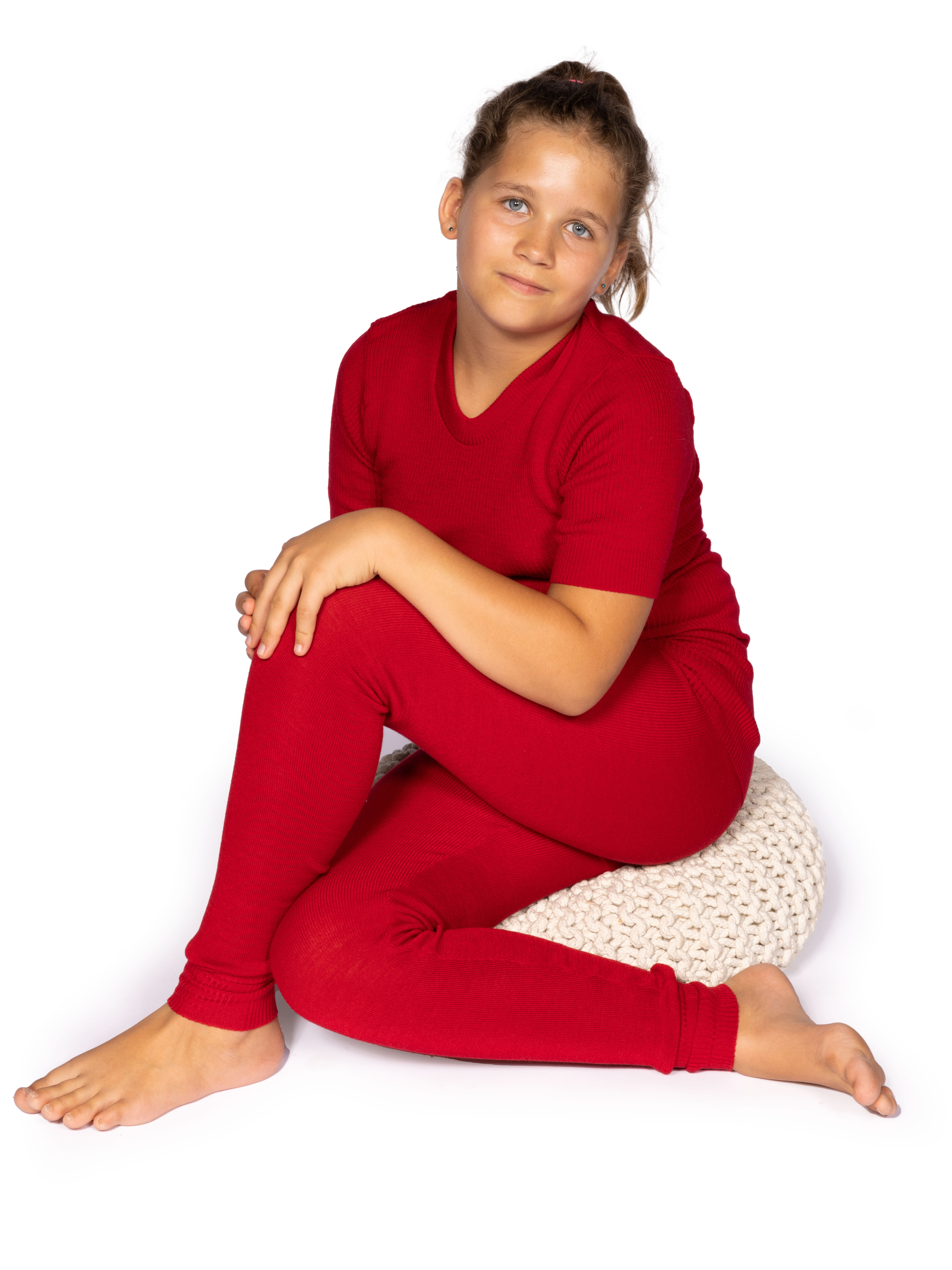 Kind in einem roten Outfit auf einem Hocker Ein Kind sitzt in einem roten Outfit auf einem gestrickten Hocker