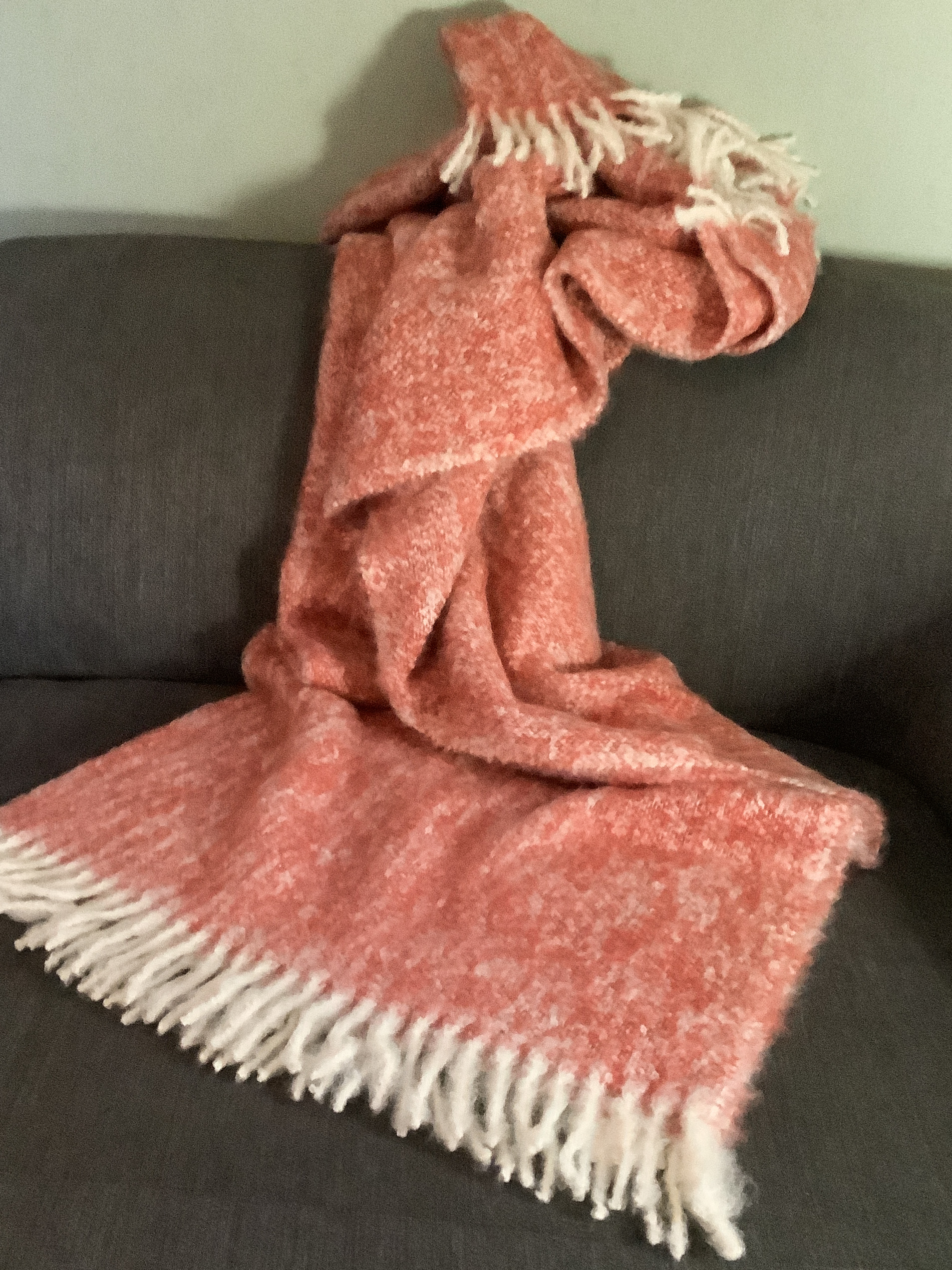 Kuschelige orange-weiße Decke mit Fransen auf Sofa Flauschige orangefarbene Decke mit weißen Fransen lässig auf einem grauen Sofa drapiert