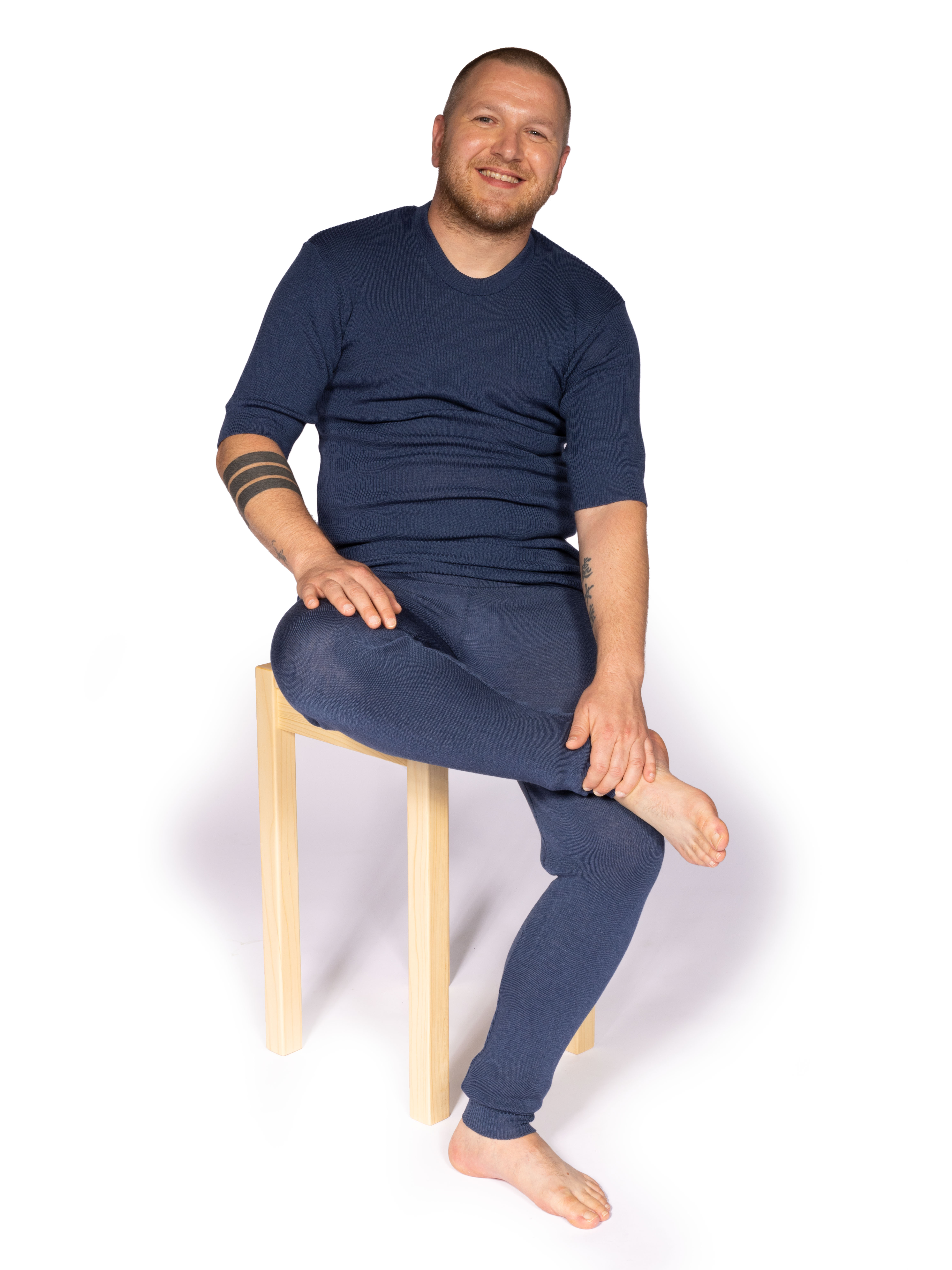 Mann in blauer Freizeitkleidung auf Holzstuhl sitzend Mann in blauer Freizeitkleidung sitzt entspannt auf einem hellen Holzstuhl