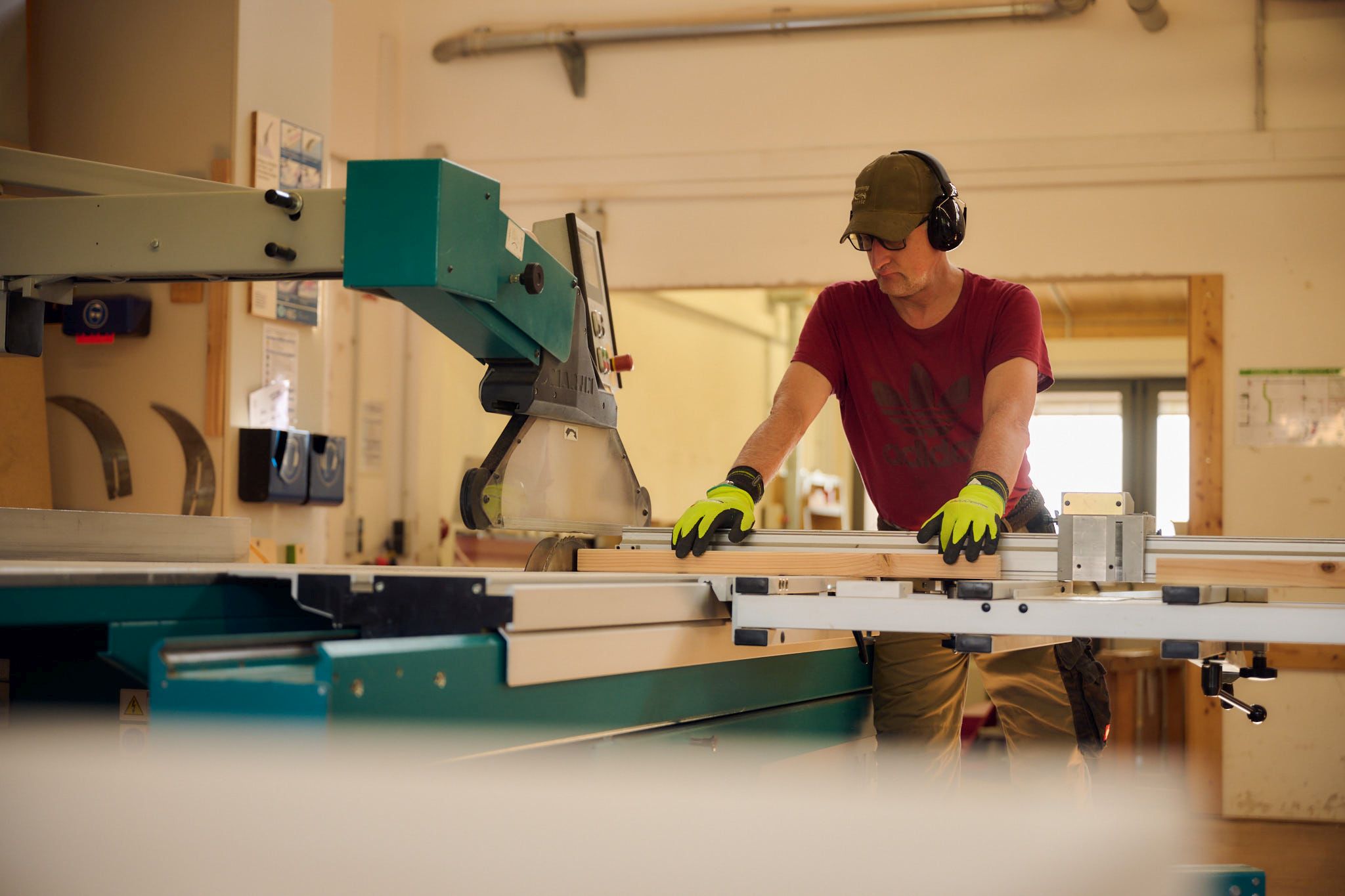 Ein Mann mit Gehörschutz und Handschuhen bedient eine Holzbearbeitungsmaschine in einer Werkstatt