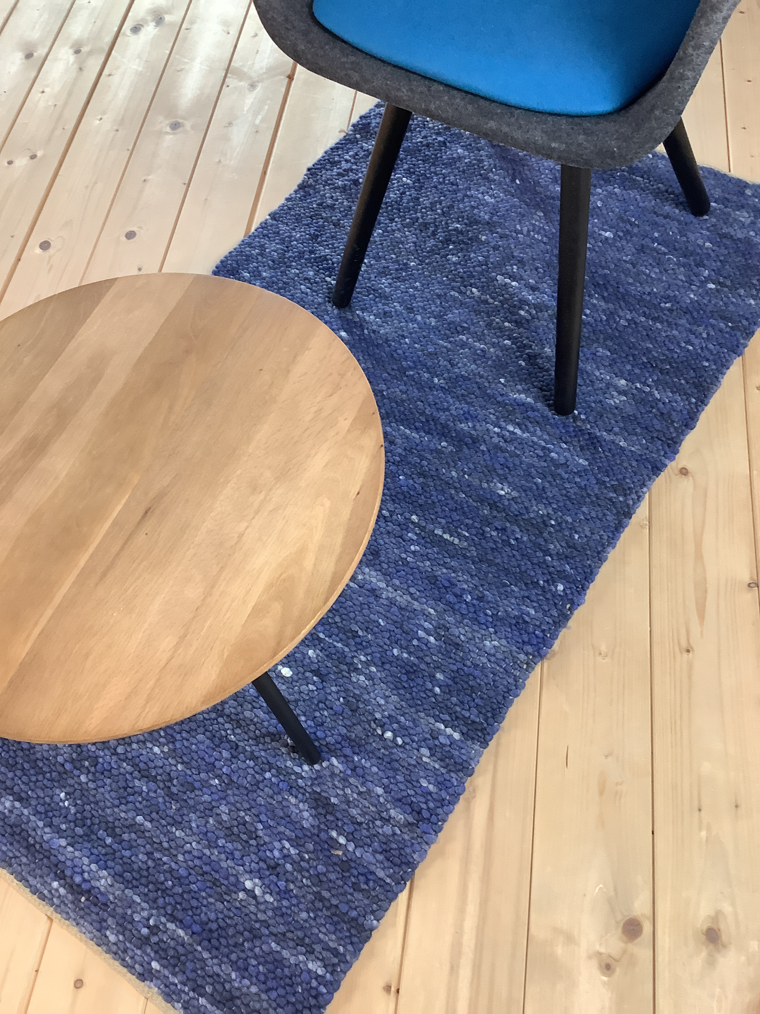Moderner Wohnbereich mit blauem Teppichläufer, rundem Beistelltisch aus Holz und gepolstertem Stuhl mit blauer Sitzfläche auf hellem Holzboden