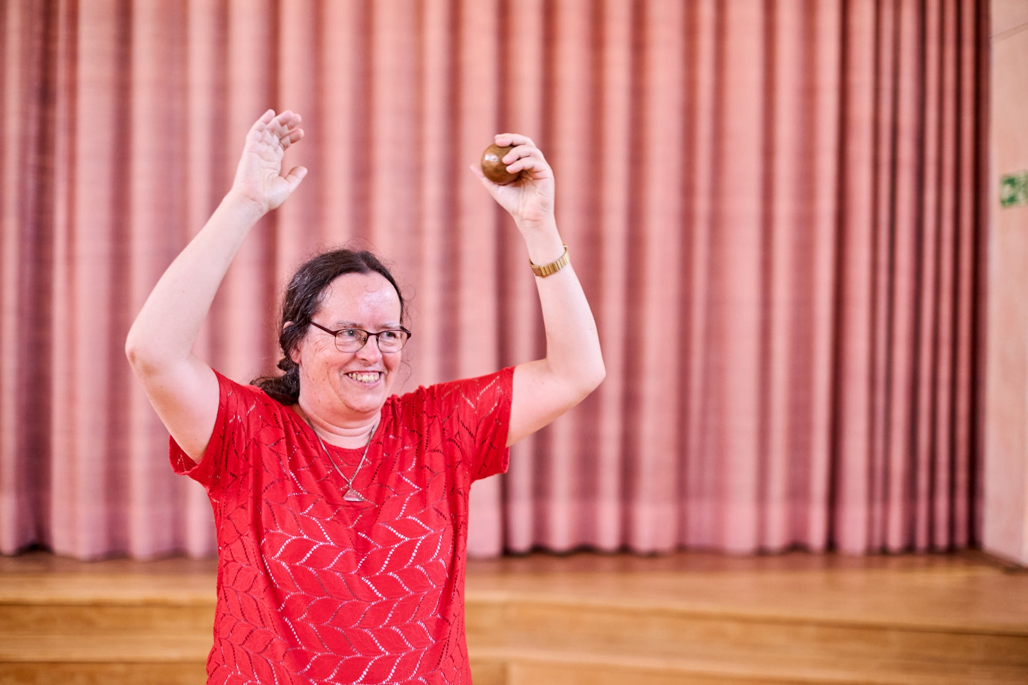 Frau in rotem Hemd hält einen Ball hoch und lächelt Eine lächelnde Frau in einem roten Hemd hebt einen kleinen Ball in einem Raum mit rosa Vorhängen hoch