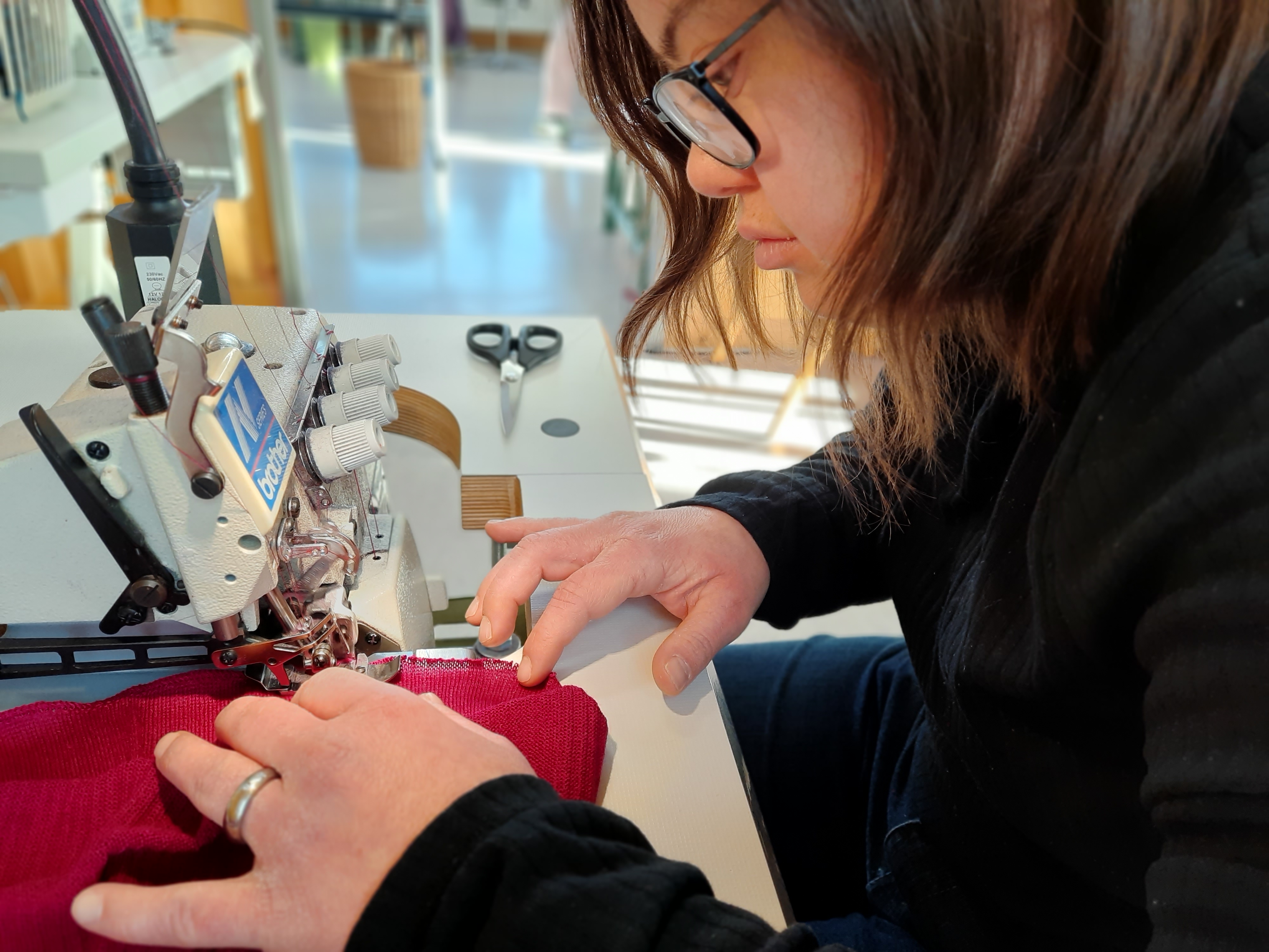 Näherin bei der Arbeit an einer Industrienähmaschine Frau näht ein rotes Kleidungsstück mit einer Industrienähmaschine