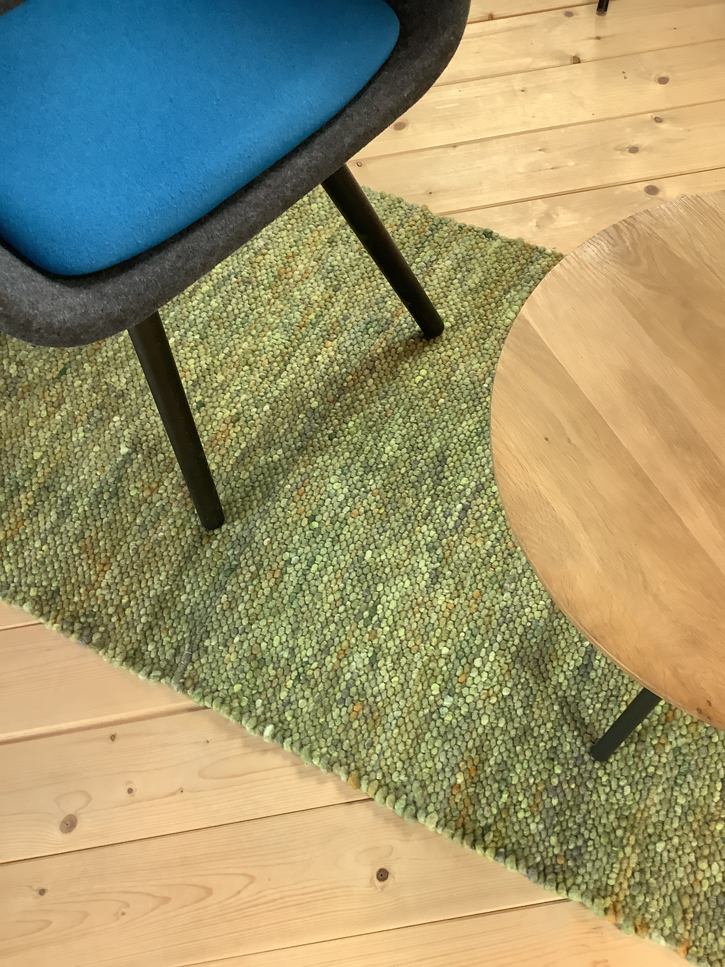 Moderner Stuhl mit blauem Sitzkissen und Holztisch auf grünem Teppich Ein moderner Stuhl mit blauem Sitzkissen steht neben einem runden Holztisch auf einem grünen Teppich, der auf einem Holzboden liegt.