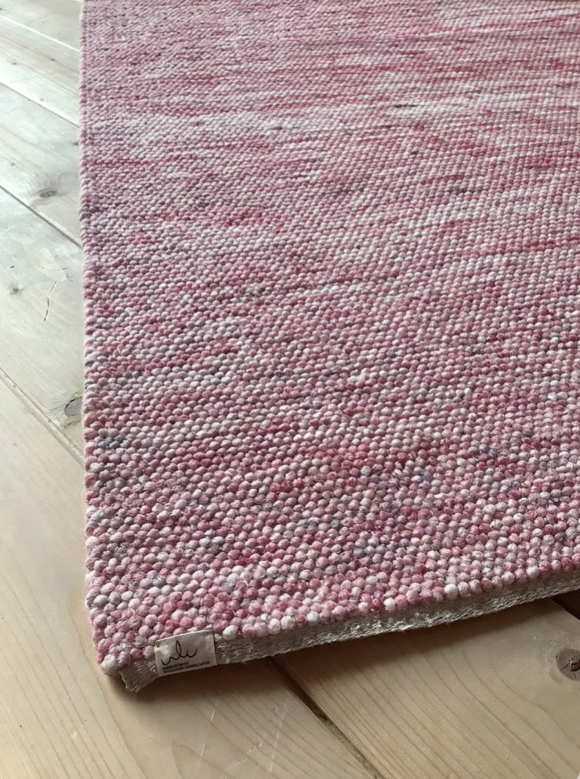Nahaufnahme eines rosafarbenen, grob strukturierten Wollteppichs auf hellem Holzboden, ideal als gemütlicher Wohnzimmerteppich