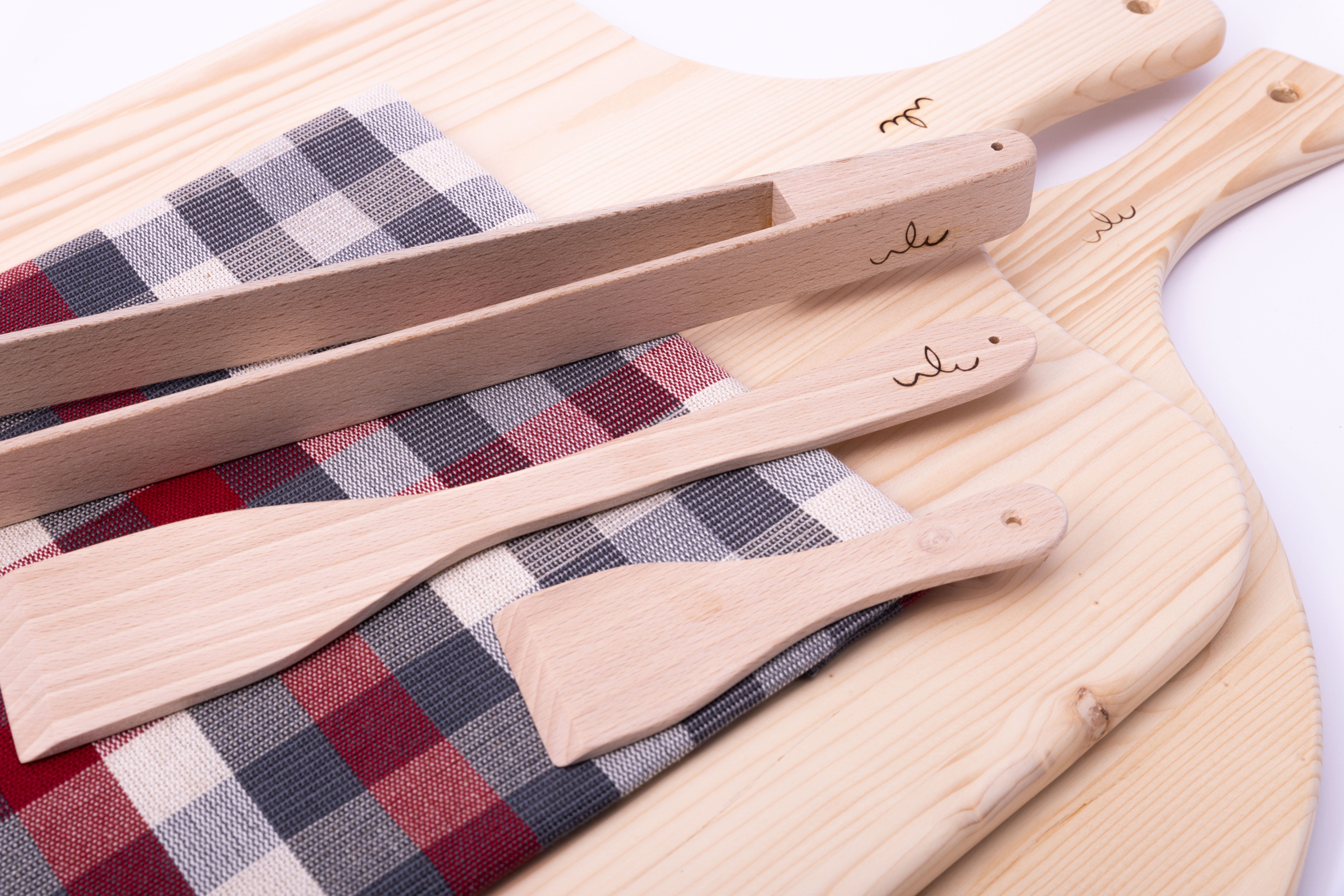 Holz-Küchenutensilien-Set auf kariertem Tuch Mehrere Holz-Küchenutensilien, inklusive Schneidebretter und Pfannenwender, liegen auf einem rot-blau-karierten Tuch