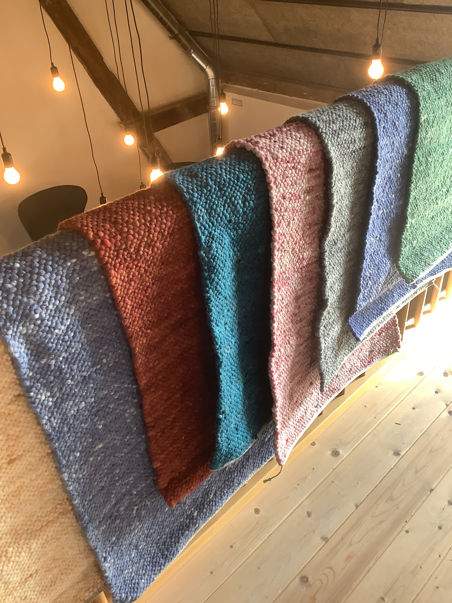 Mehrere handgestrickte Wolldecken in verschiedenen Farben hängen dekorativ über einem Holzgeländer in einem gemütlichen Raum