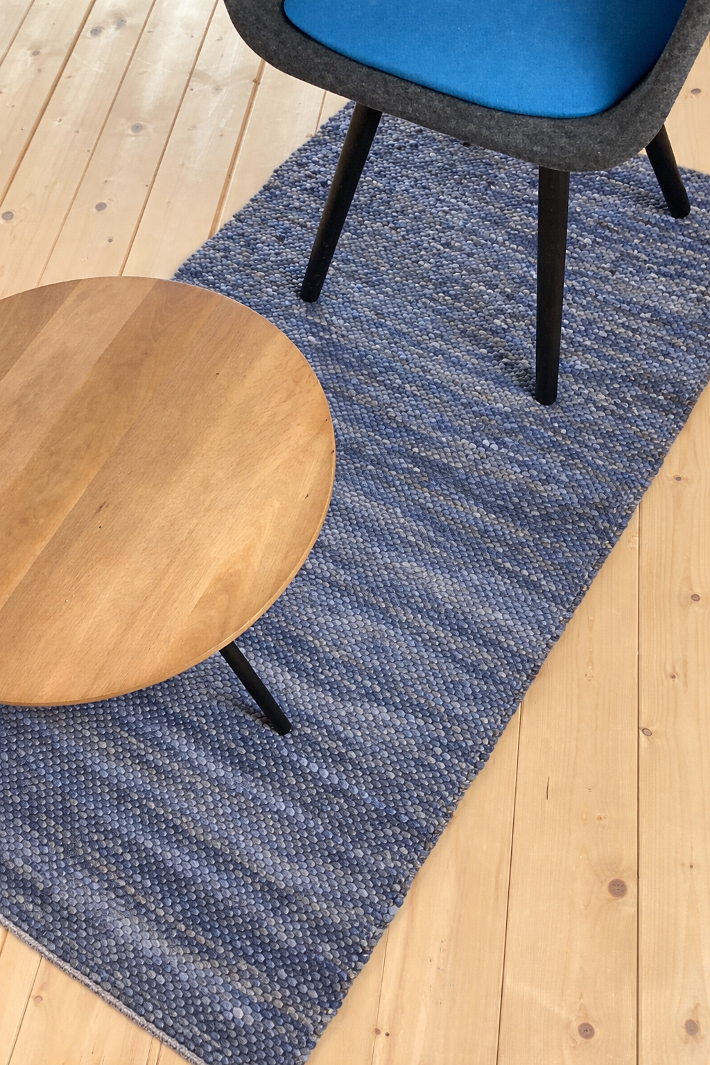 Rechteckiger blau melierter Webteppich auf hellem Holzboden, dekoriert mit rundem Holztisch und modernem Stuhl in skandinavischem Stil