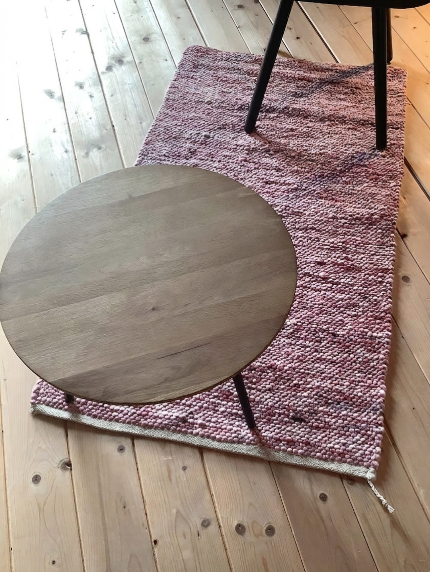 Runder Holztisch mit schwarzen Beinen steht auf einem rosa Teppich aus Wollkügelchen auf hellem Holzboden