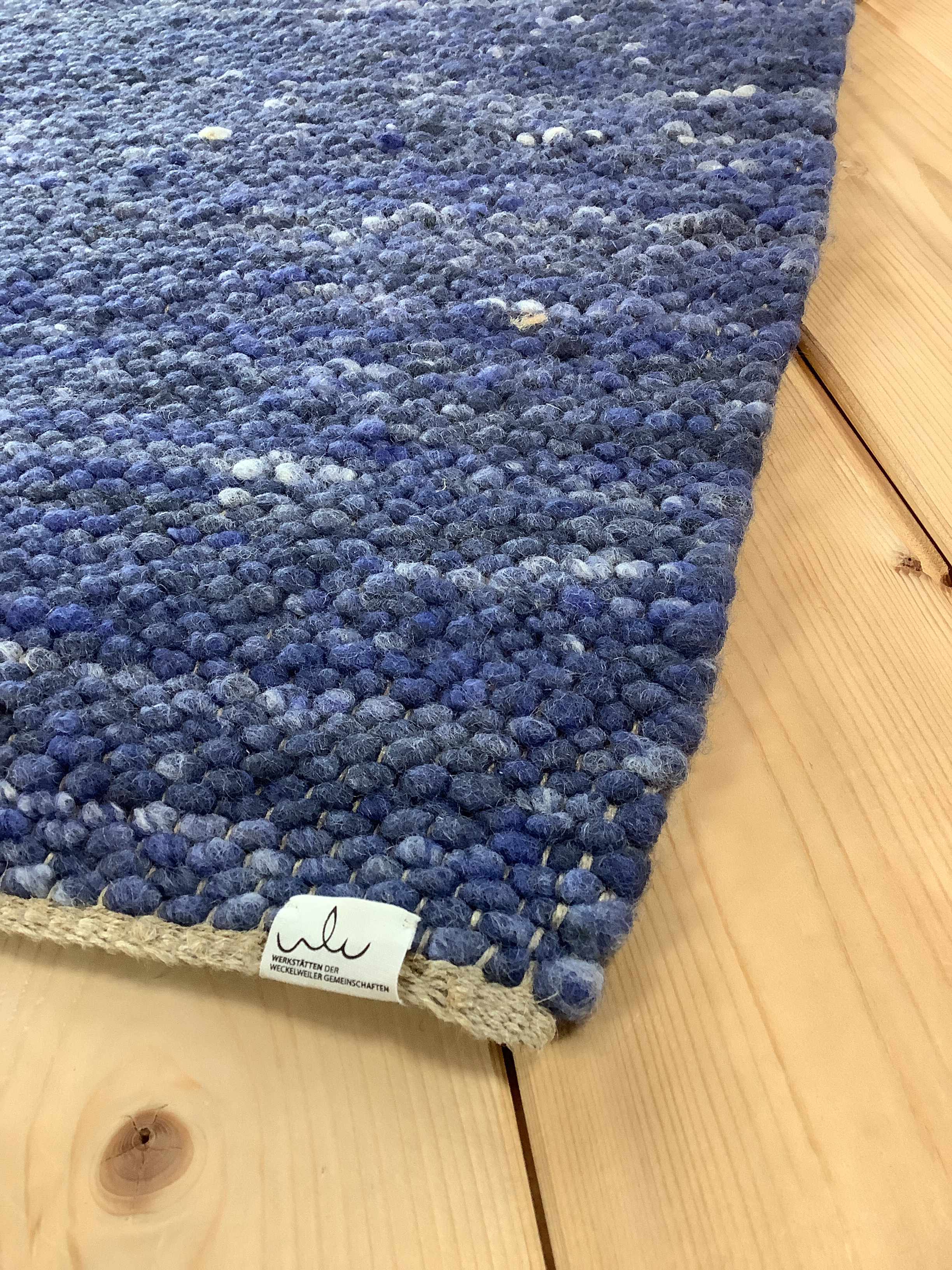 Blauer handgewebter Teppich aus Wolle auf Holzboden Nahaufnahme eines blauen handgewebten Wollteppichs auf einem Holzboden