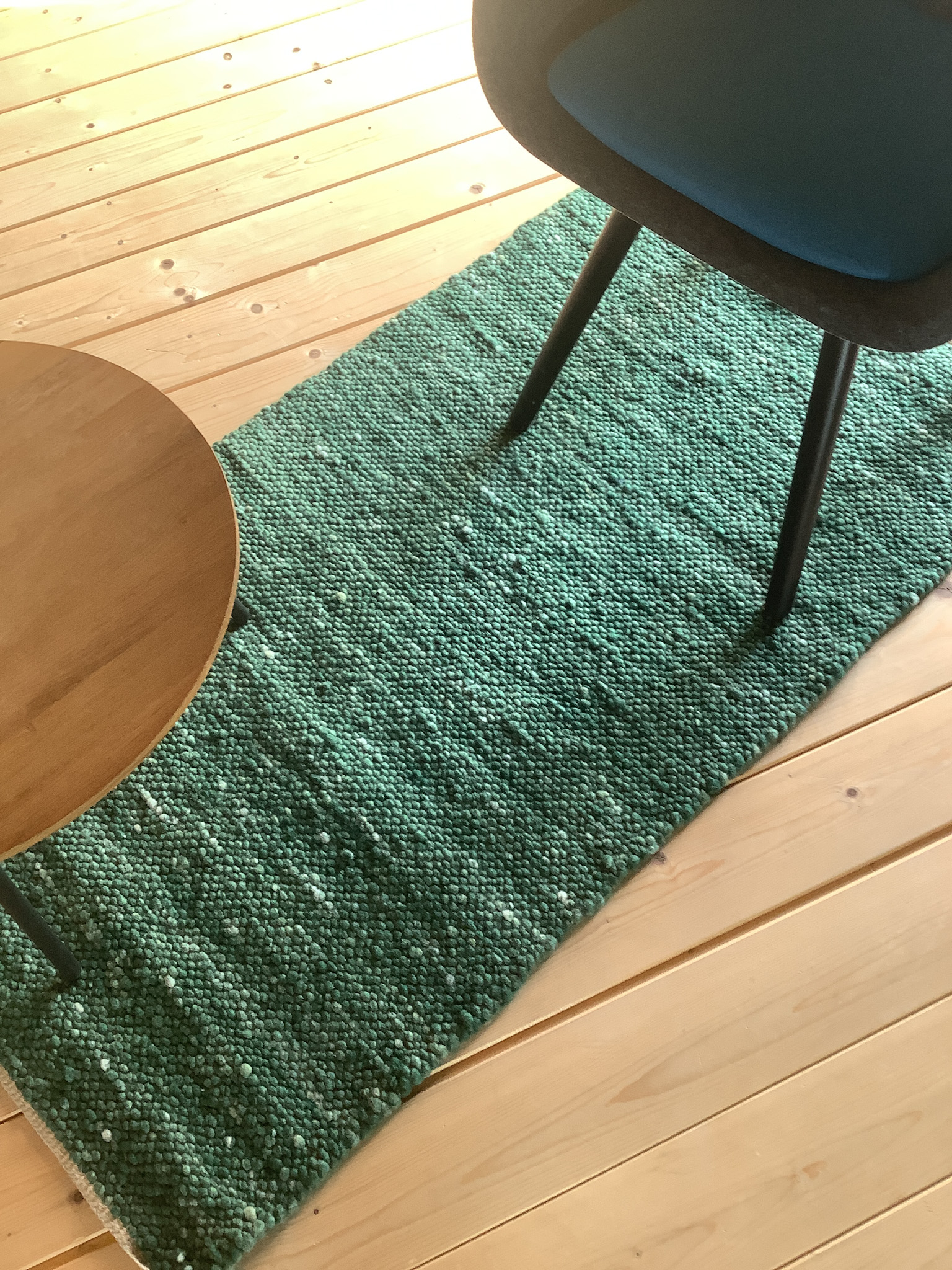 Schmaler grüner Woll-Läufer auf hellem Holzboden, daneben ein moderner Stuhl und ein runder Beistelltisch