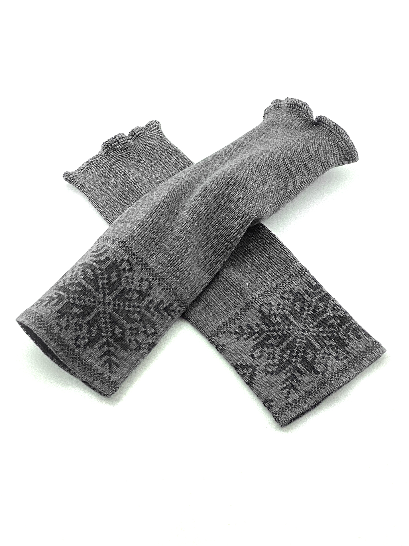 Graue gestrickte Stulpen mit Schneeflockenmuster Ein Paar graue gestrickte Stulpen mit dekorativem Schneeflockenmuster liegend auf weißem Hintergrund