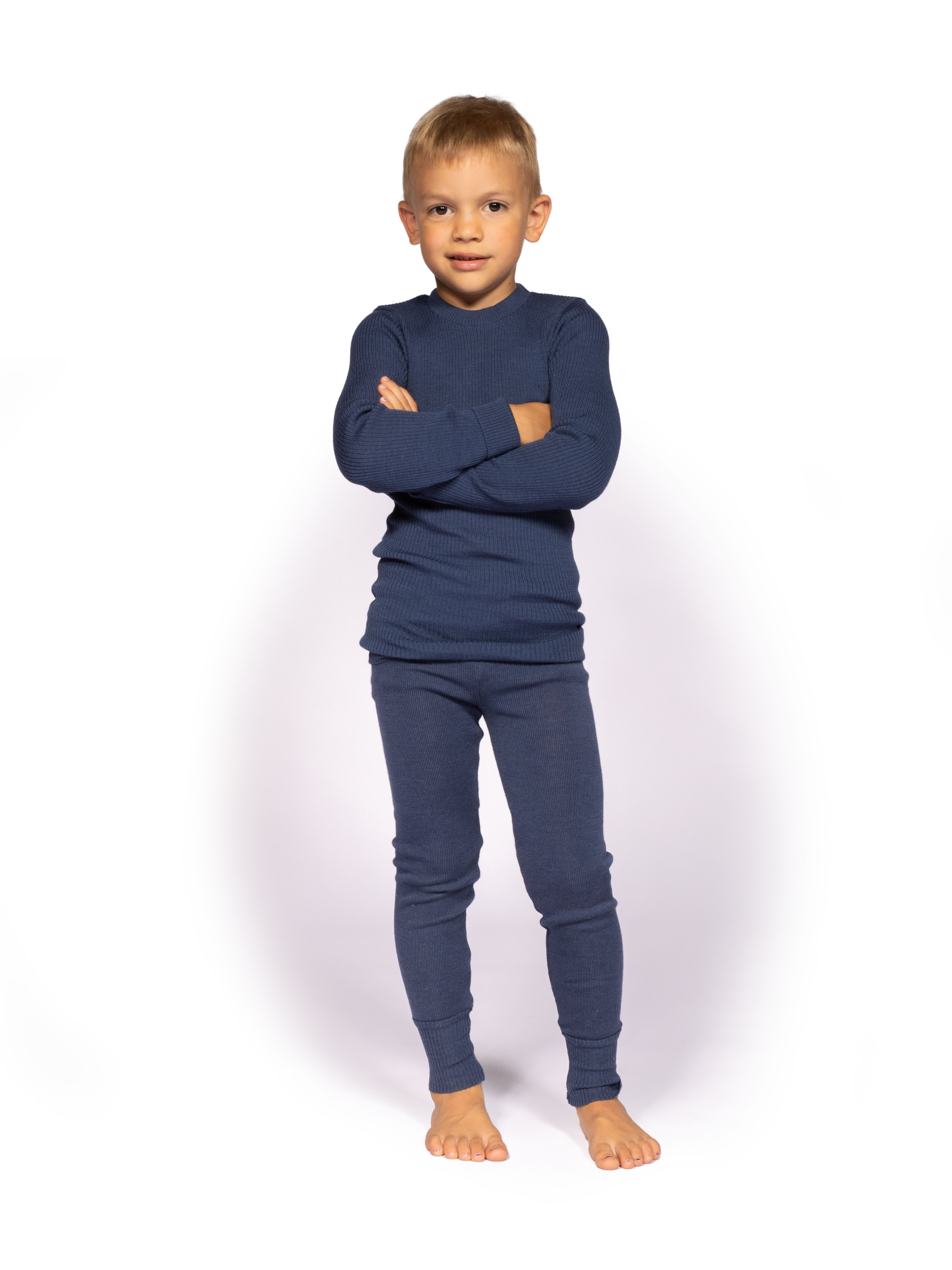 Junge in dunkelblauer Kinderunterwäsche aus Wolle Ein Junge trägt dunkelblaue Kinderunterwäsche aus Wolle und steht mit verschränkten Armen auf einem weißen Hintergrund.