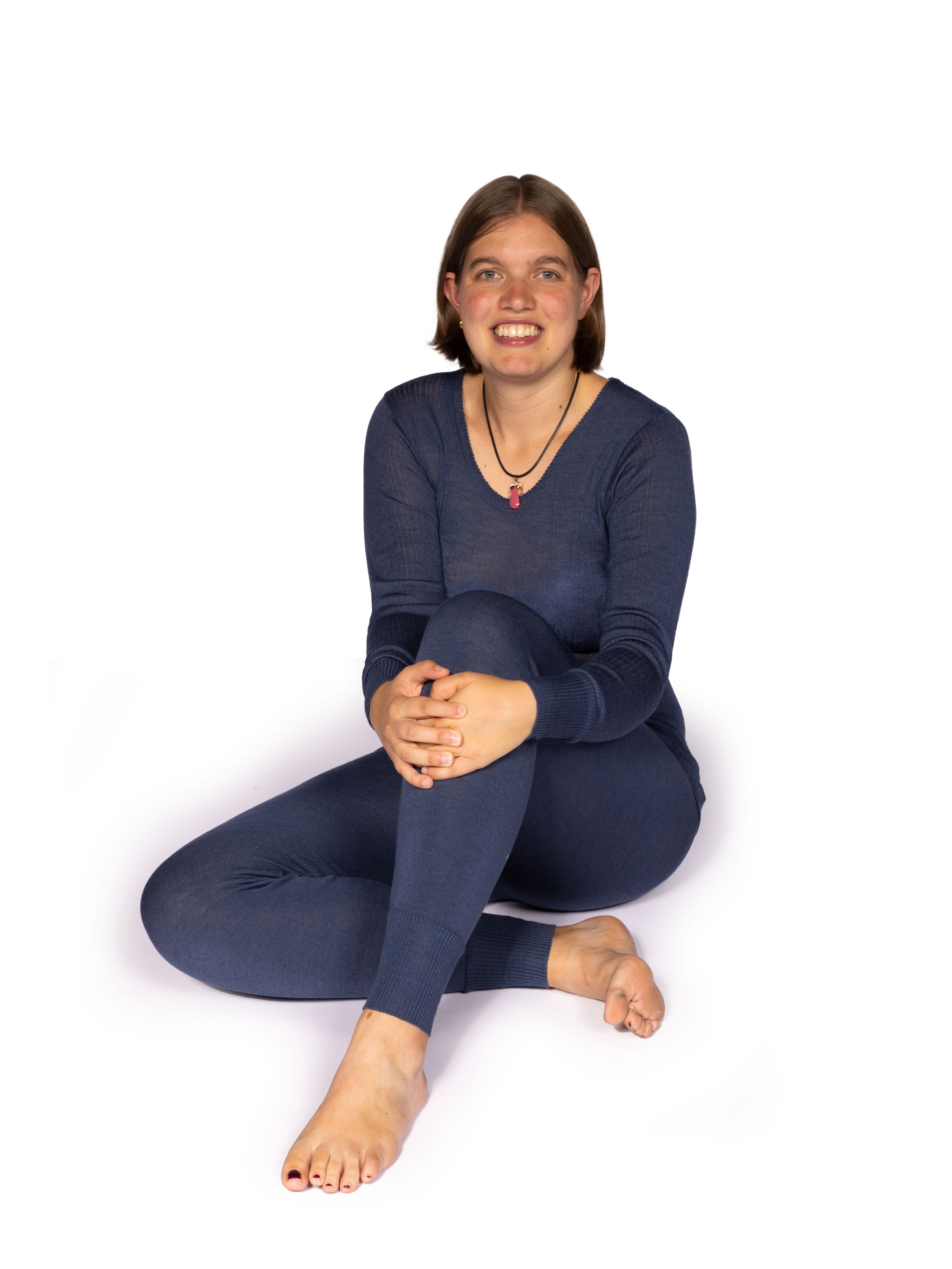 Lächelnde Frau in dunkelblauen Leggings und Shirt sitzt barfuß auf dem Boden