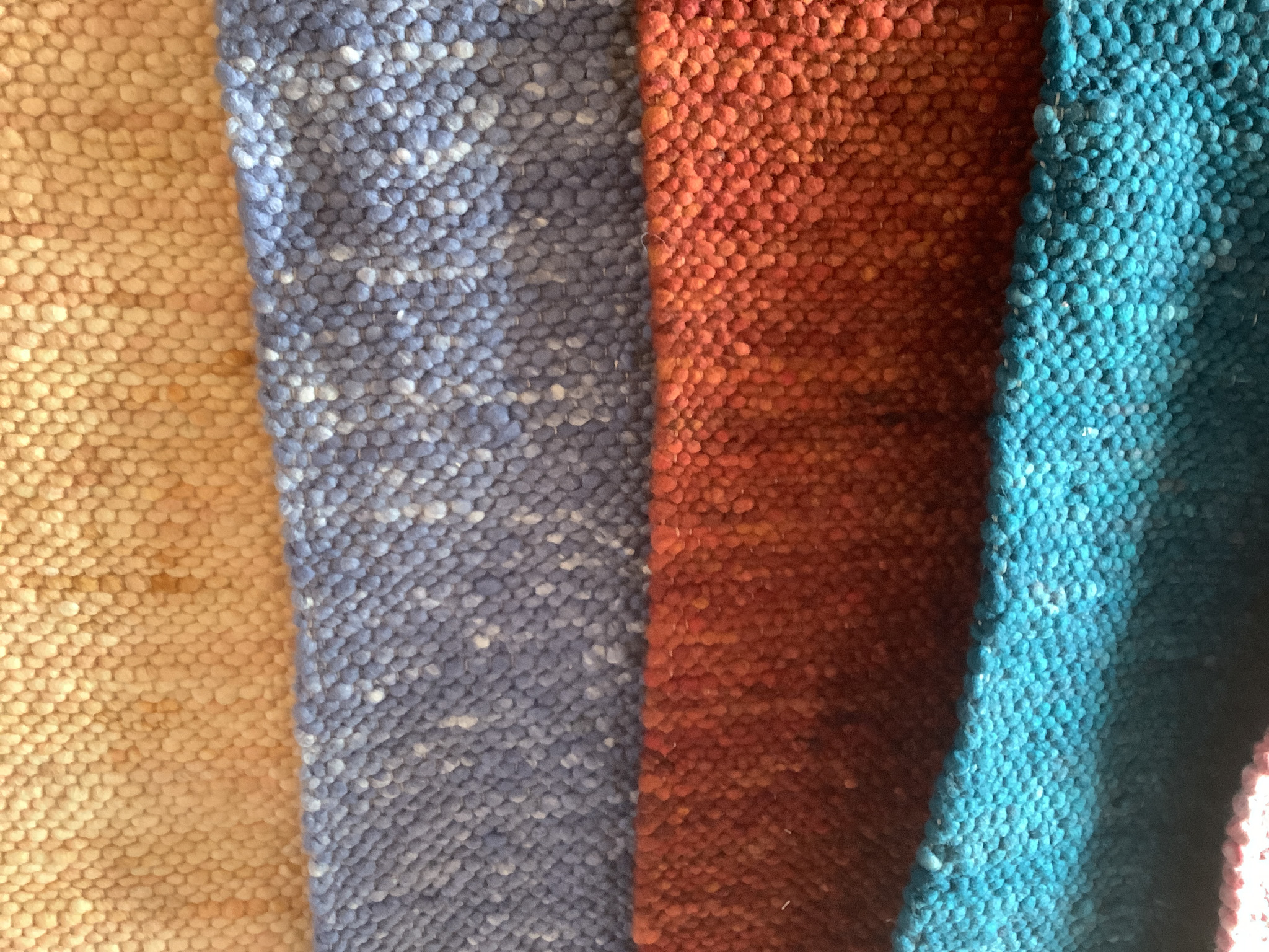 Detailansicht eines handgewebten Teppichs mit grober Struktur in Beige, Blau, Rot und Türkis