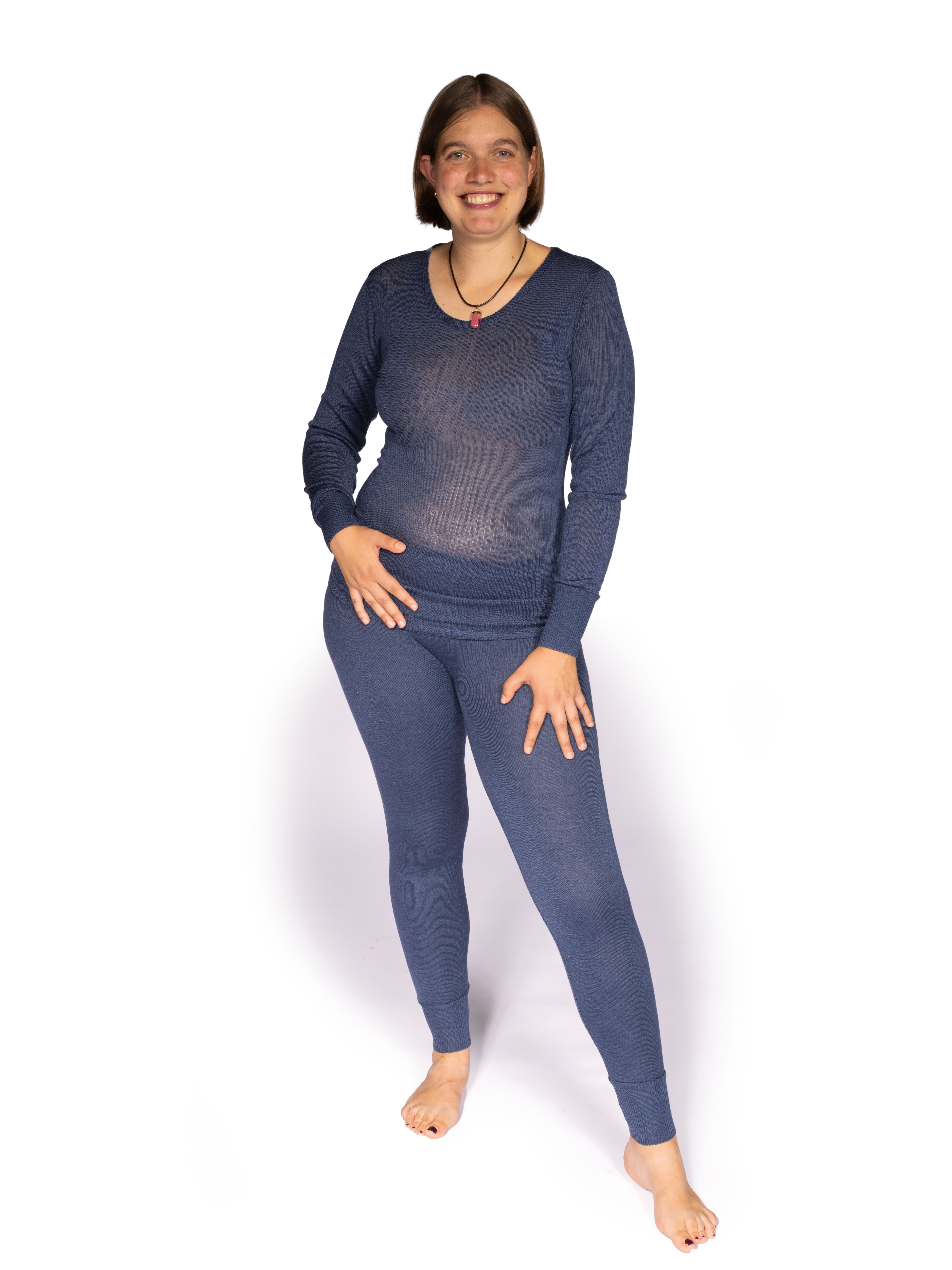 Frau trägt blaue Damen-Thermounterwäsche, bestehend aus langärmligem Oberteil und Leggings, barfuß auf weißem Hintergrund