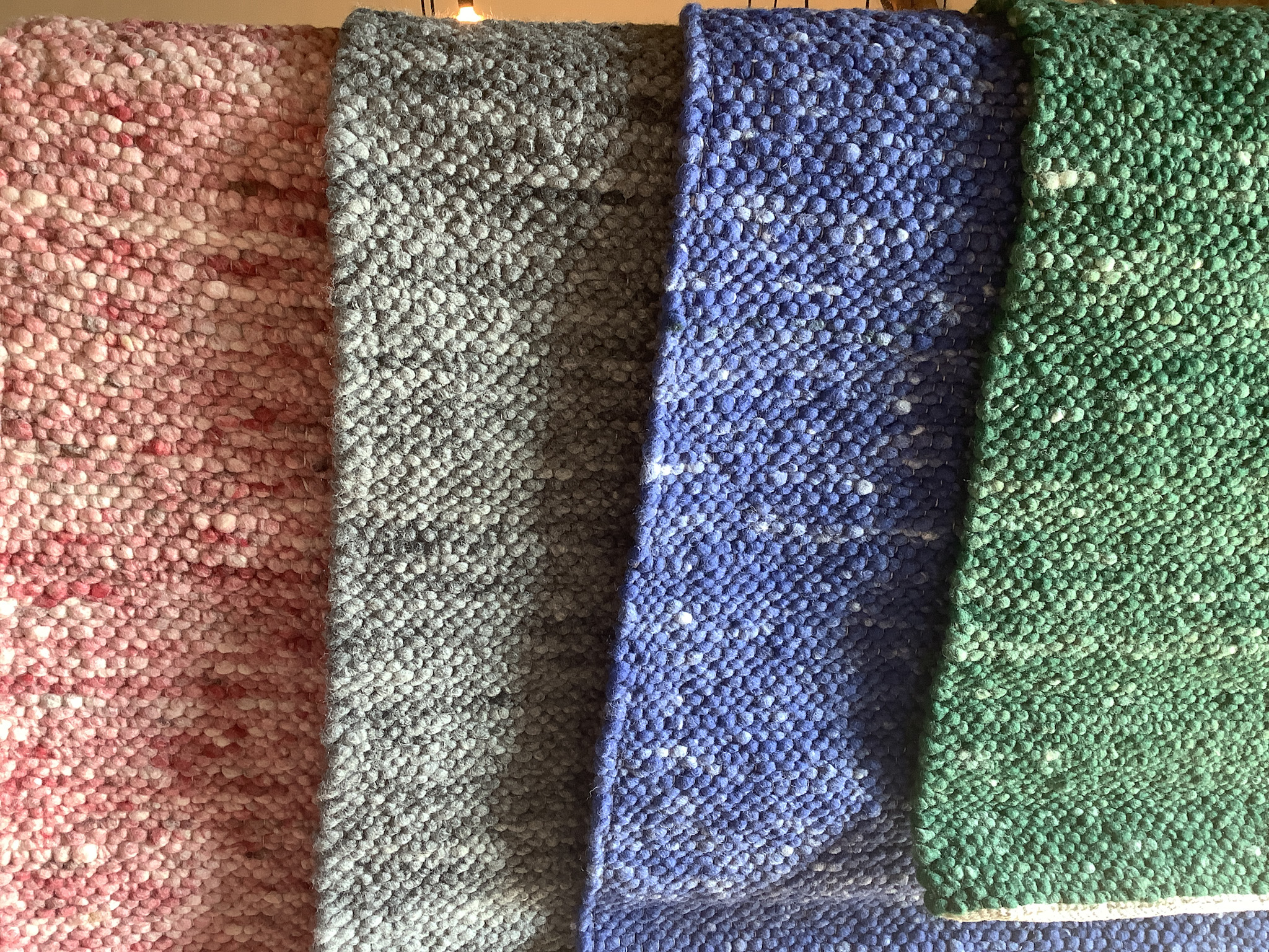 Nahaufnahme von vier handgewebten Wollteppichen in Rosa, Grau, Blau und Grün mit grober Struktur