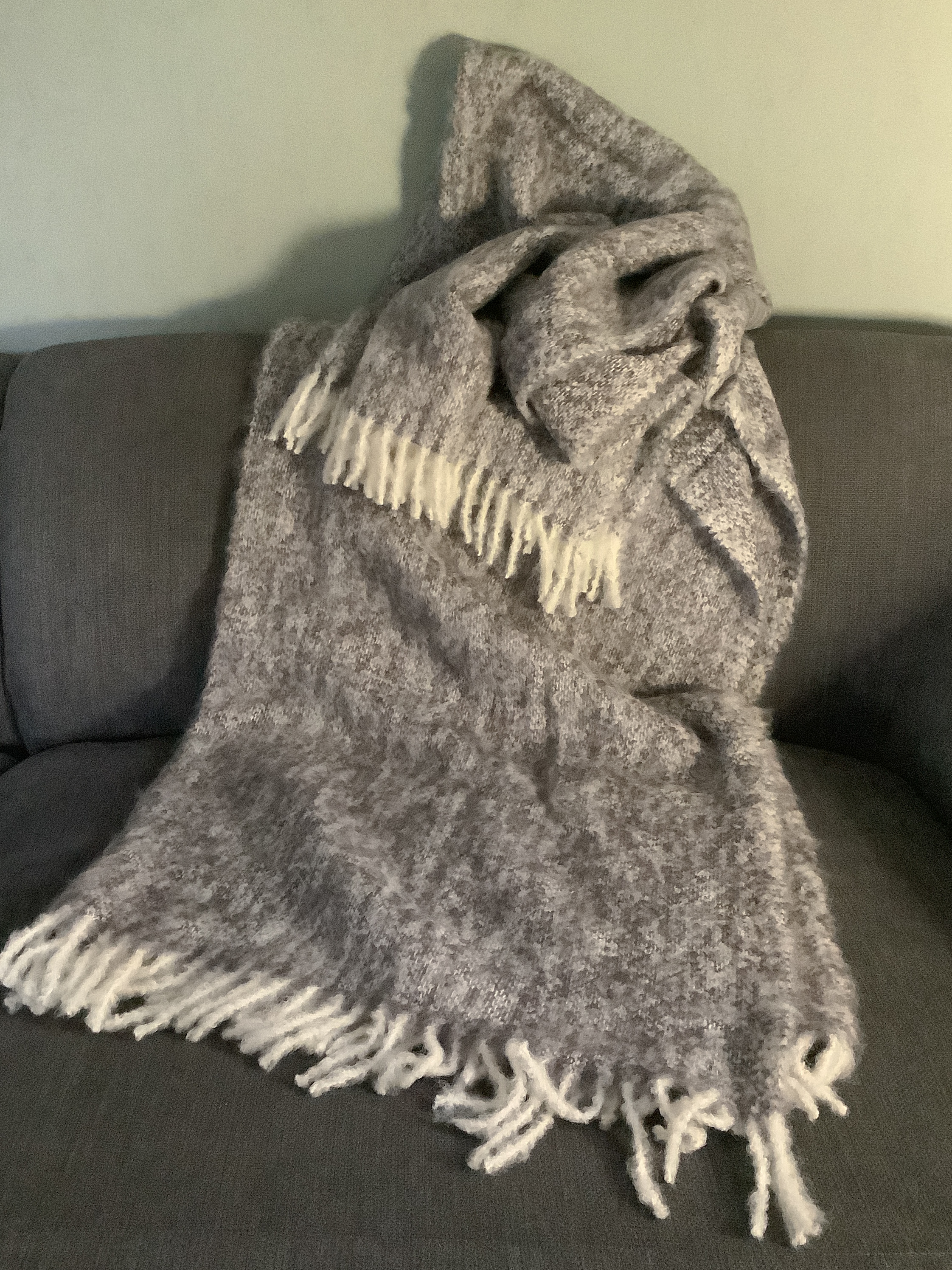 Weiche graue Kuscheldecke mit Fransen auf einem Sofa Graue Kuscheldecke mit Fransen auf einem Sofa drapiert