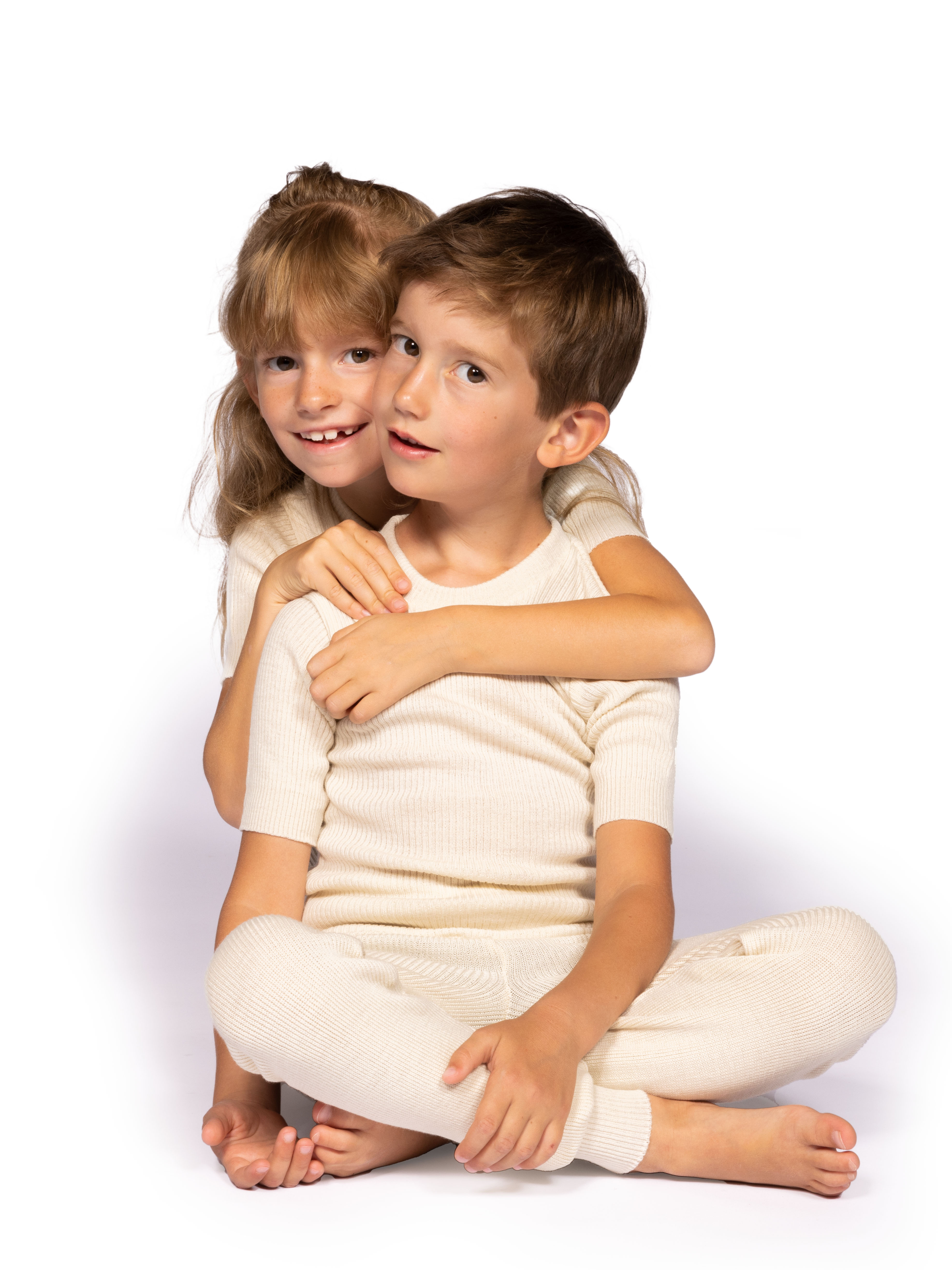 Kinder in gemütlicher, cremefarbener Baumwollbekleidung Zwei Kinder in bequemer, cremefarbener Freizeitkleidung aus Baumwolle, die miteinander spielen und Spaß haben.