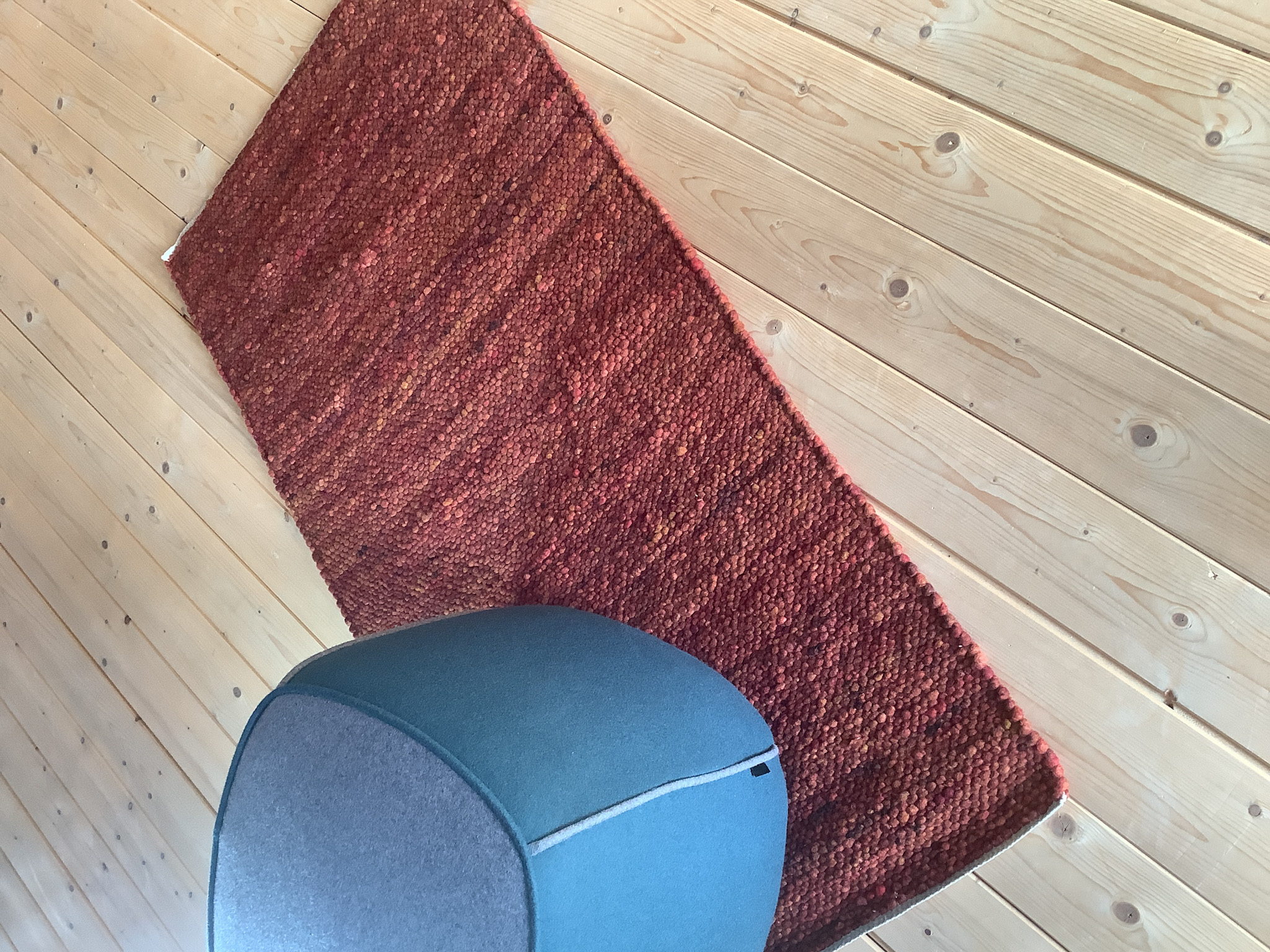 Kleiner handgewebter roter Wollteppich auf hellem Holzboden mit modernem gepolstertem Hocker