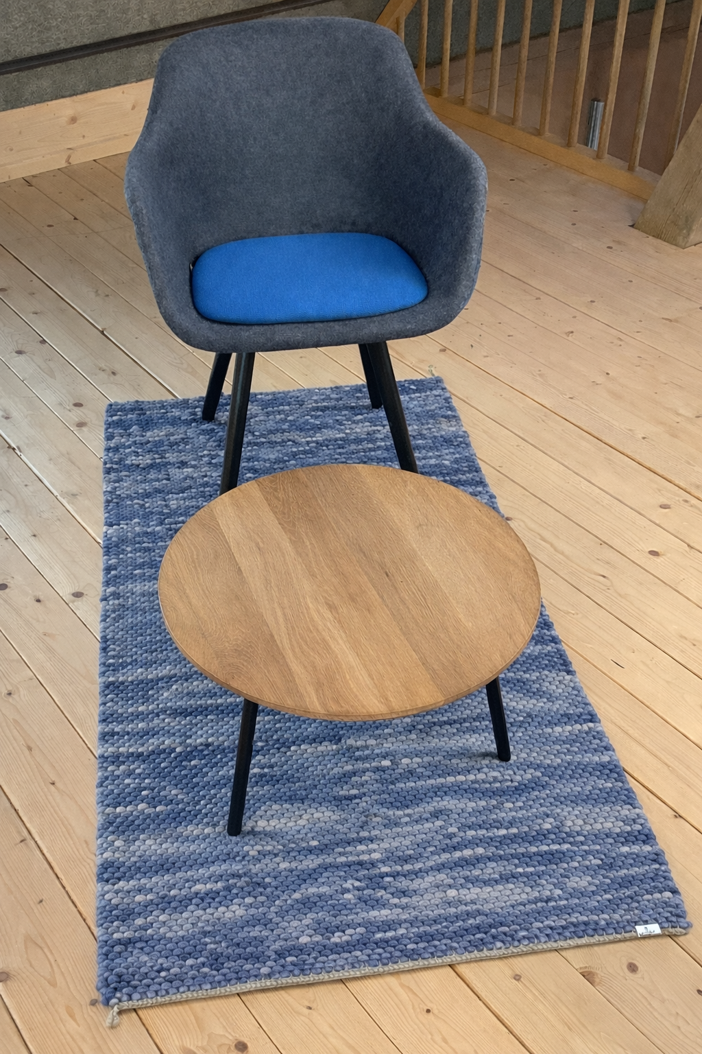 Moderner, handgewebt wirkender Wollteppich in Blau- und Grautönen auf hellem Holzboden, dekoriert mit grauem Stuhl und rundem Holzcouchtisch