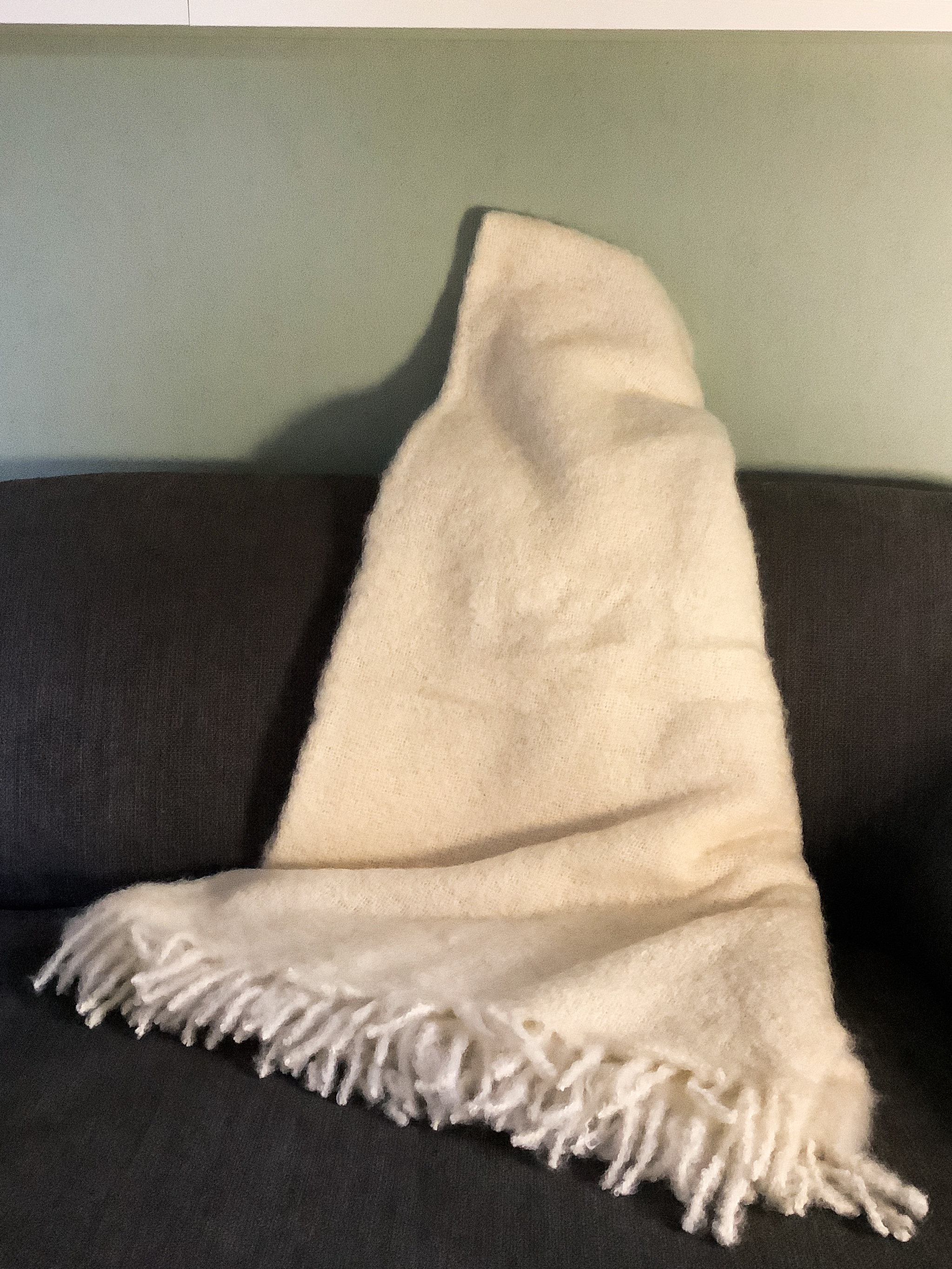 Weiche cremefarbene Decke mit Fransen auf dem Sofa Weiche cremefarbene Decke mit Fransen auf einem grauen Sofa drapiert