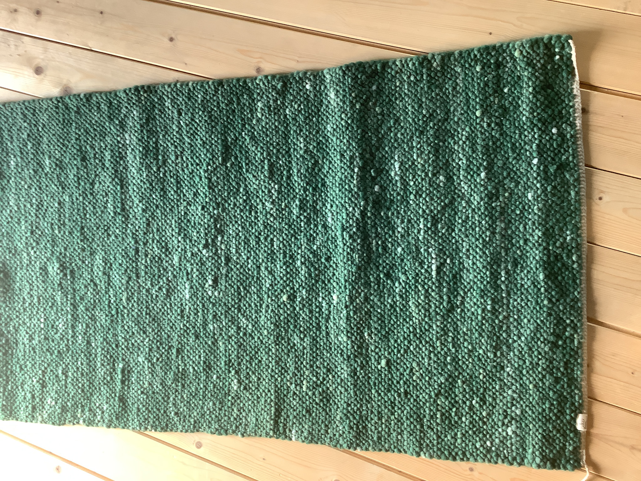 Rechteckiger, grün melierter Wollteppich im Läuferformat auf hellem Holzboden, grob gewebte Struktur