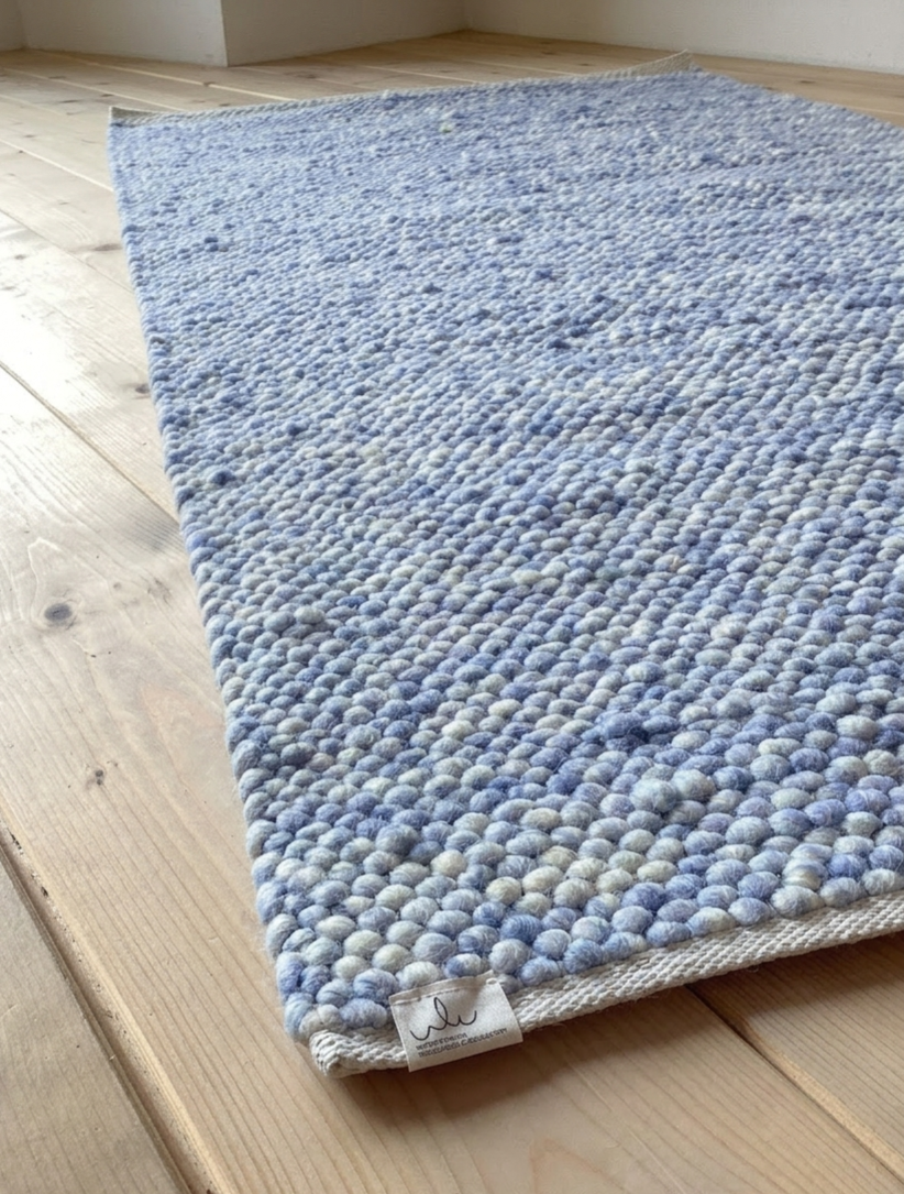 Nahaufnahme eines handgewebten hellblauen Wollteppichs mit strukturierter Oberfläche auf hellem Holzboden, ideal für Wohnzimmer oder Schlafzimmer