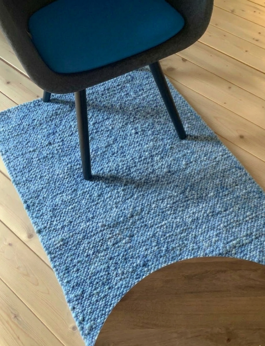 Rechteckiger, blau melierter Wollteppich auf hellem Holzboden, dekoriert mit modernem Stuhl und rundem Holztisch im skandinavischen Einrichtungsstil