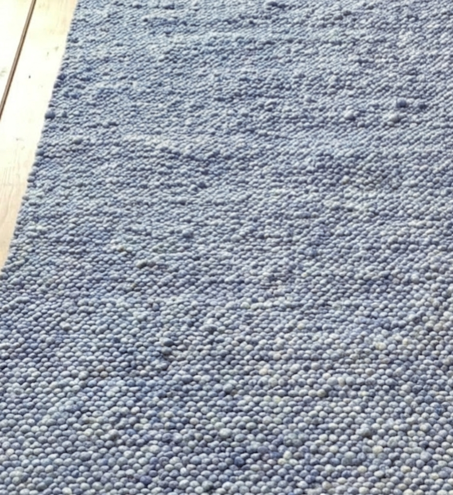Detailansicht eines hellblauen, grob strukturierten Wollteppichs auf hellem Holzboden, moderner Skandi-Stil