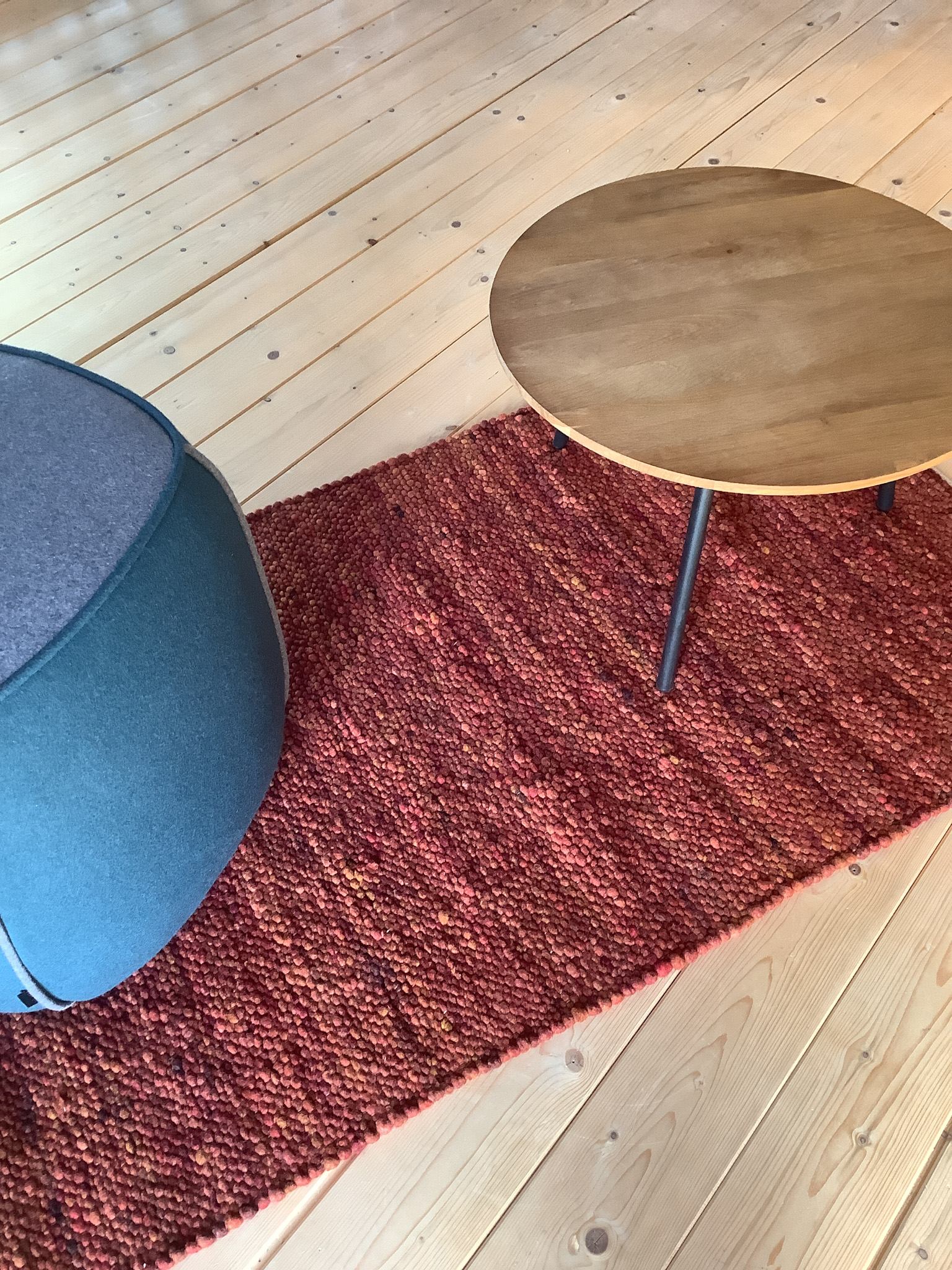 Roter, strukturierter Läufer auf hellem Holzboden mit rundem Holzcouchtisch und modernem Hocker