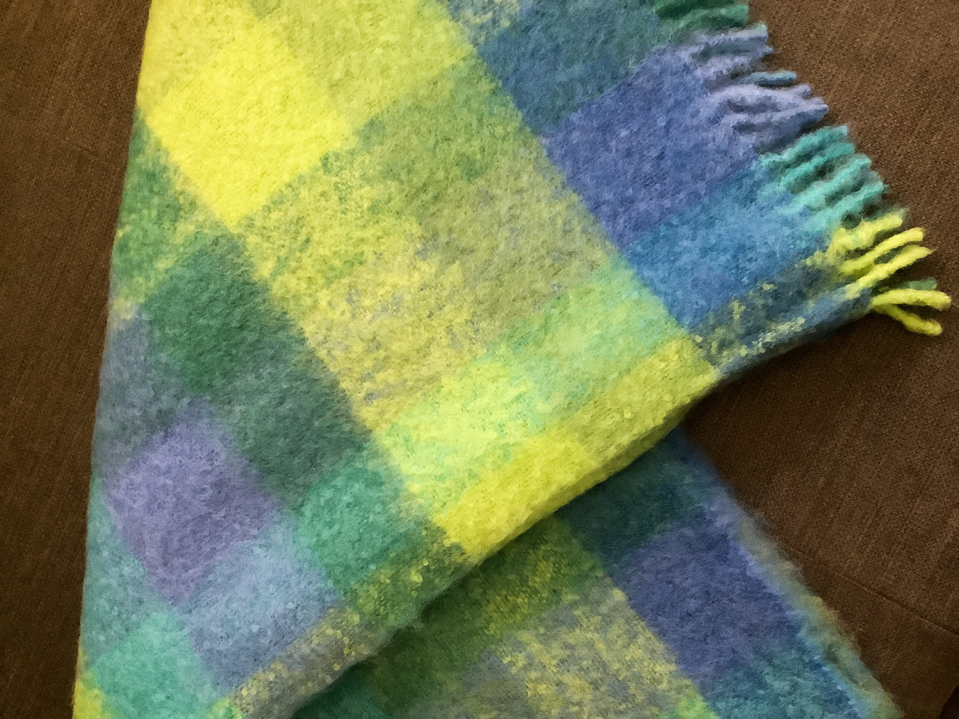 Warme Decke mit buntem Karomuster Bunte Decke mit Karomuster in Grün-, Blau- und Gelbtönen auf braunem Hintergrund