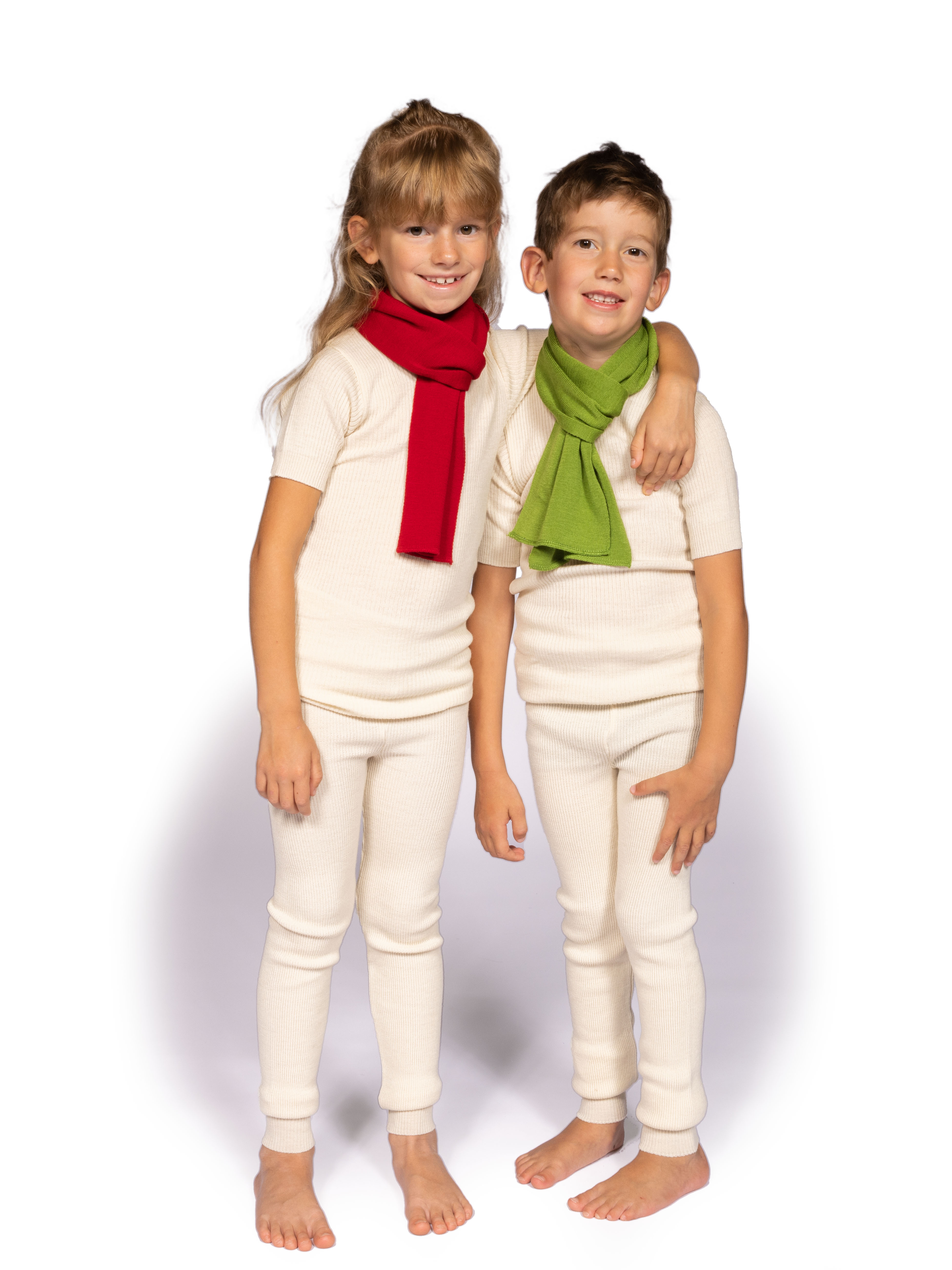 Zwei Kinder tragen weiße Thermounterwäsche und bunte Schals, ein roter und ein grüner, und stehen nebeneinander.