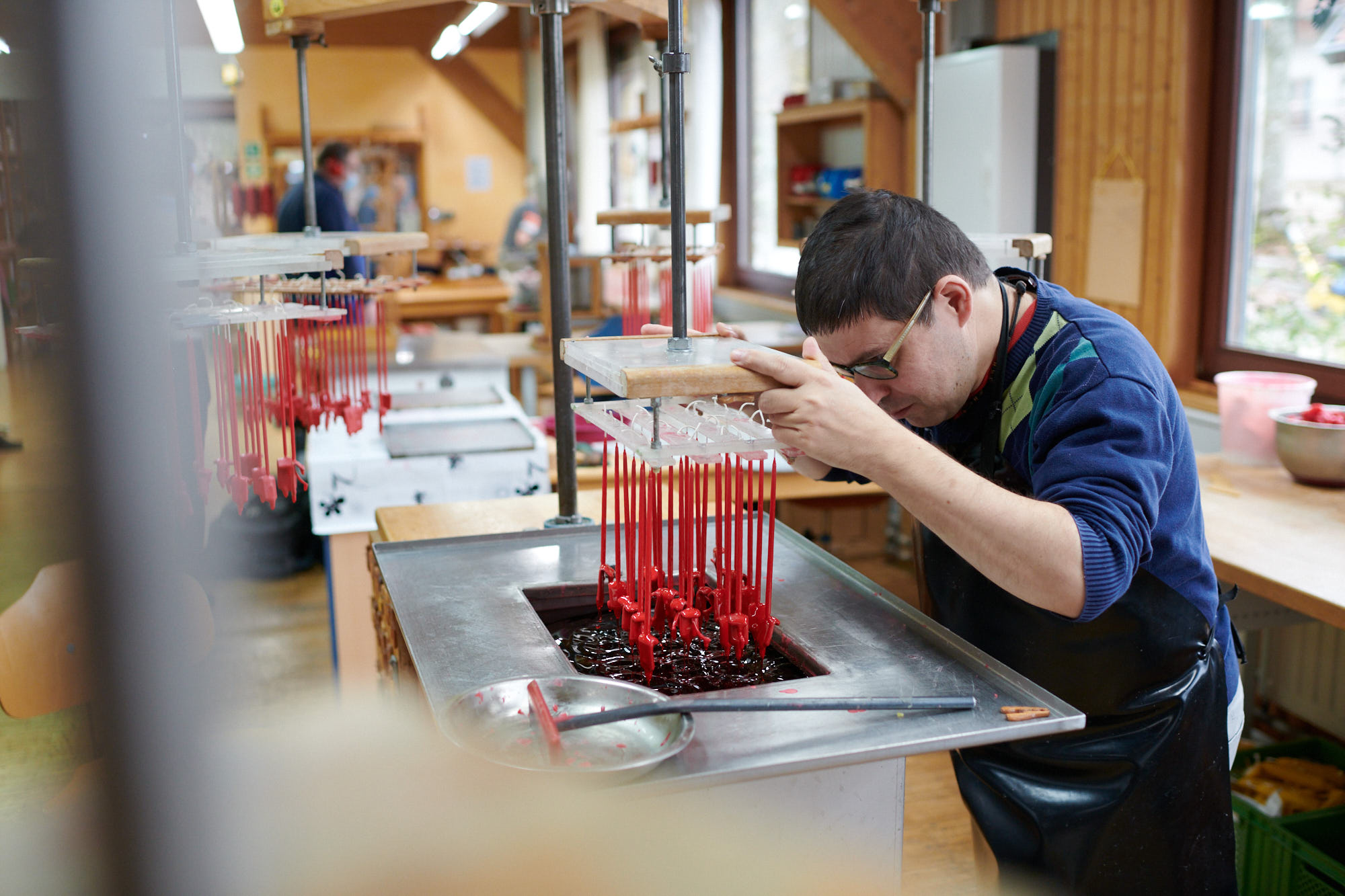 Handwerker bei der Kerzenherstellung in einer Werkstatt Mann in einer Werkstatt bei der Herstellung von Kerzen, rote Wachsstangen in einem Behälter