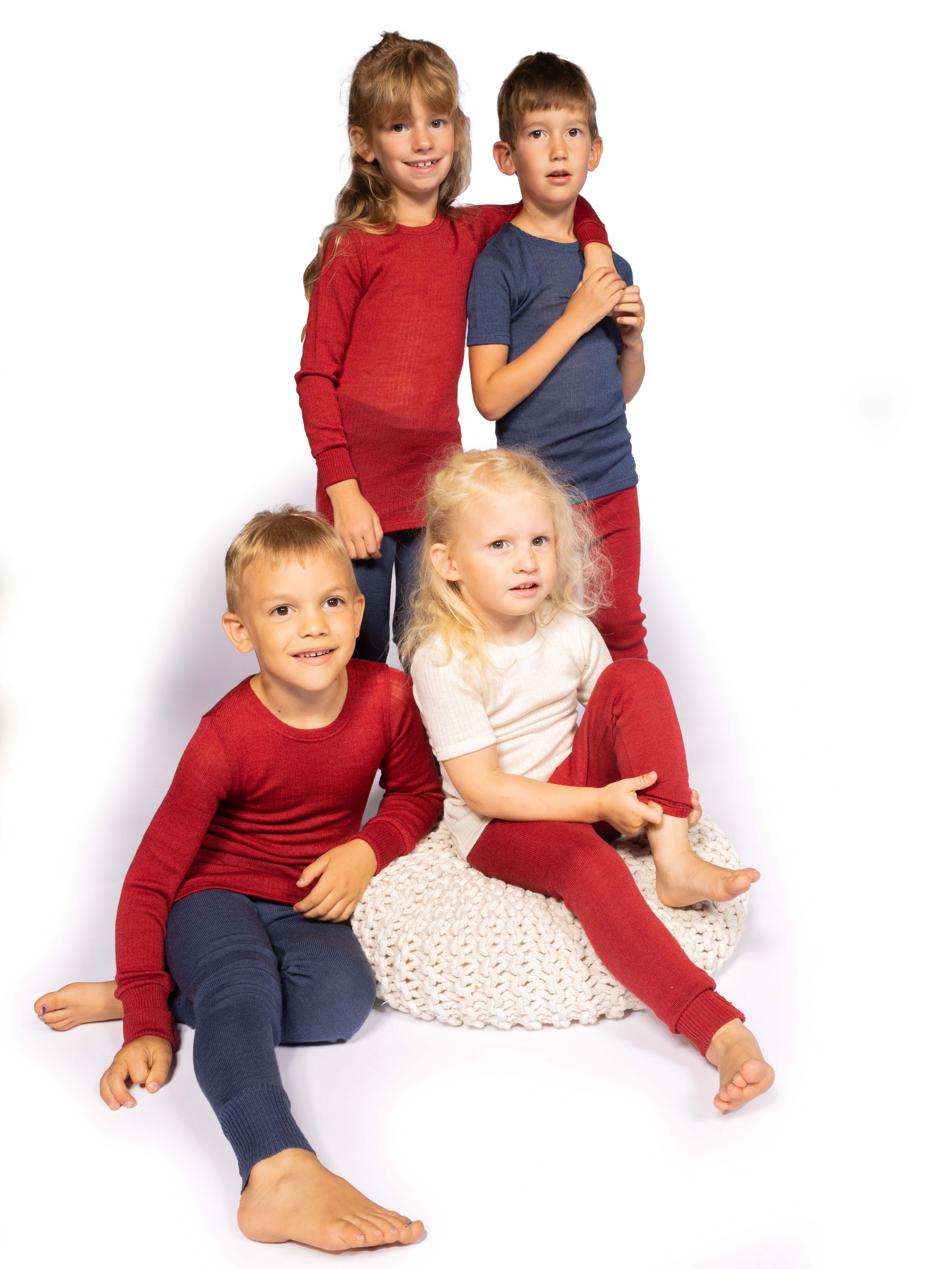 Gruppe von vier Kindern in farbenfrohen Outfits; zwei Kinder stehen und zwei sitzen auf einem weißen Polster