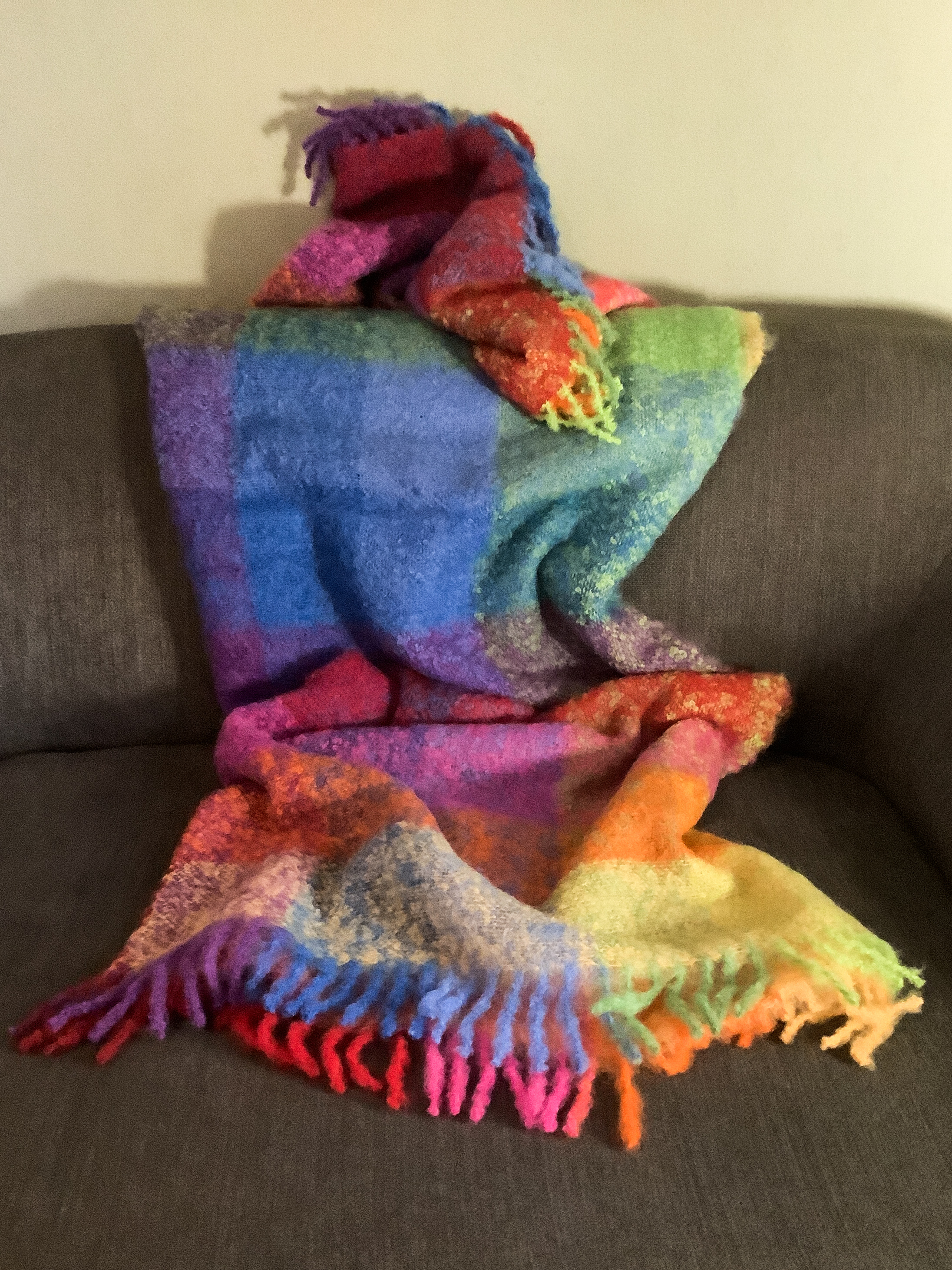 Kuschelige Regenbogen-Decke auf Sofa Bunte, kuschelige Decke in Regenbogenfarben auf einem grauen Sofa drapiert