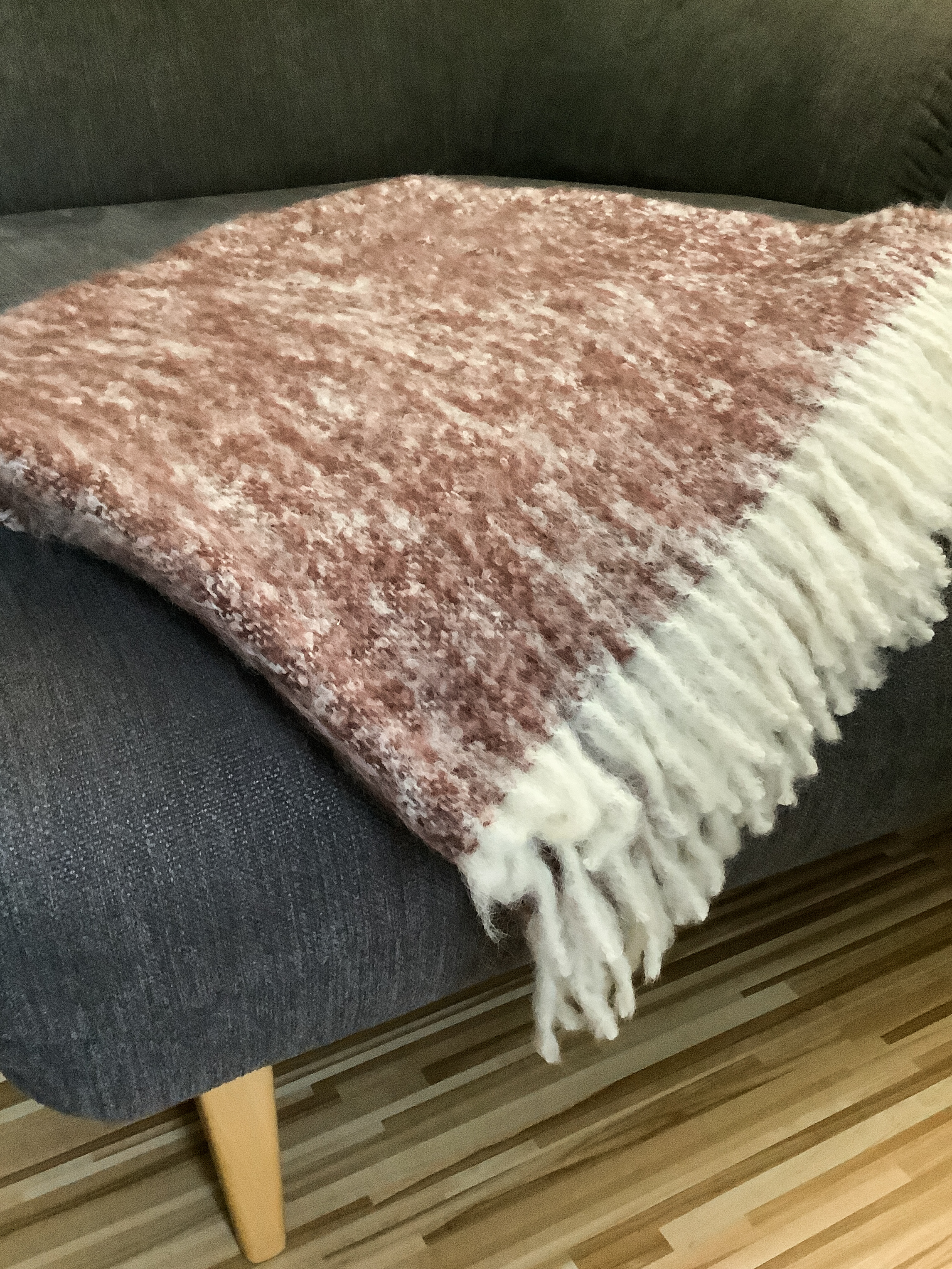 Weiche Kuscheldecke in Rosa und Weiß auf Sofa Rosa-weiße Kuscheldecke mit Fransen liegt auf grauem Sofa im Wohnzimmer