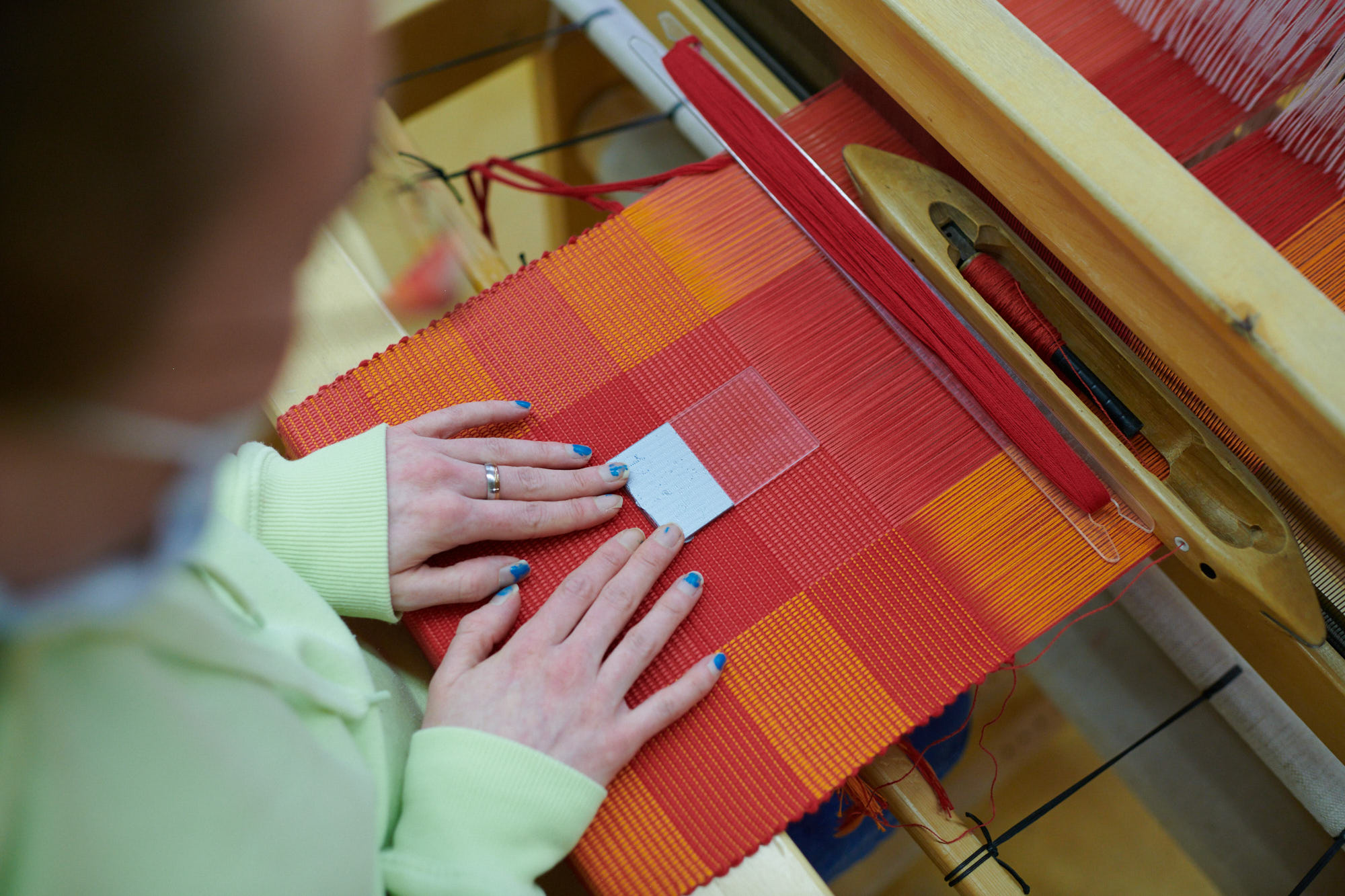 Handgefertigte Textilweberei an einem Webstuhl Nahaufnahme einer Person, die an einem Webstuhl ein rot-oranges Textilgewebe herstellt